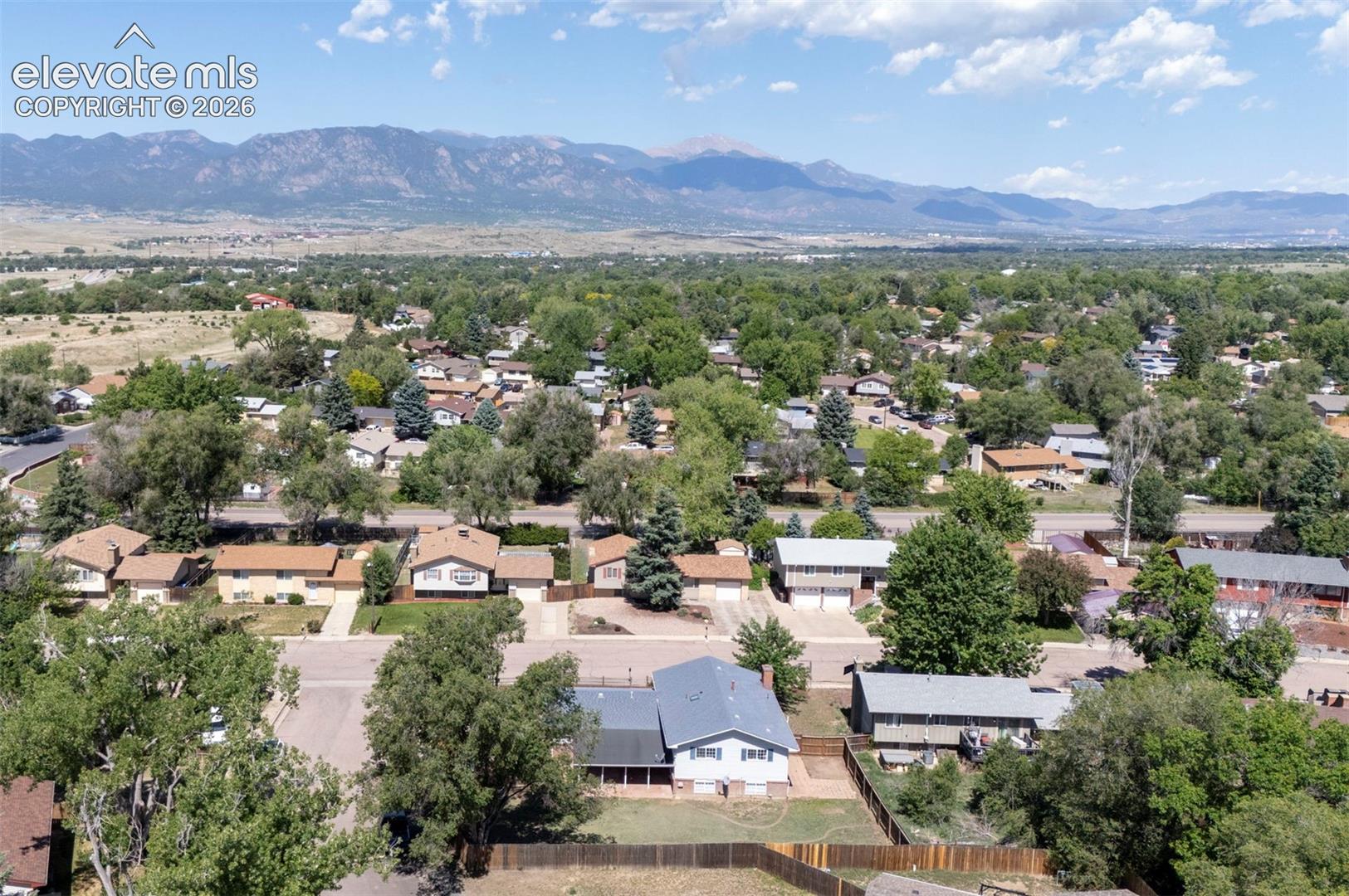 Aerial perspective featuring a multi-level residential structure with a shingled roof, an attached garage, a fenced backyard, and mountain range scenery