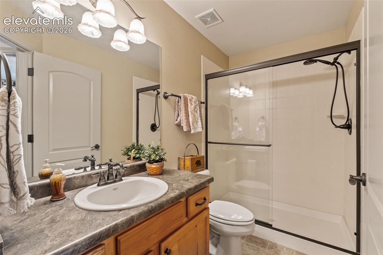 Bathroom featuring a wood-finish vanity with an oval undermount sink, a countertop with a stone-look finish, a mirrored wall, and an enclosed shower with a dark-framed sliding glass door