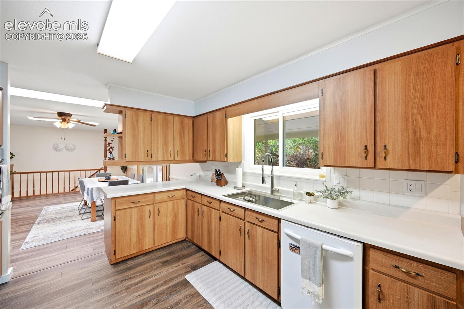 Kitchen featuring wood-finish cabinetry, solid surface countertops, a white subway tile backsplash, and a stainless steel undermount sink with a gooseneck faucet