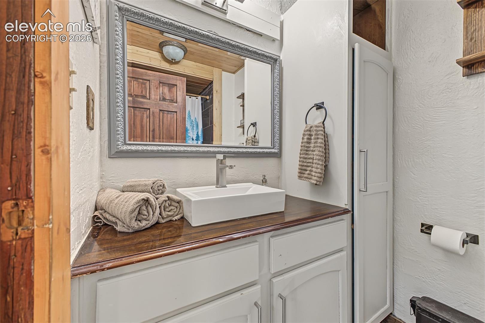White vanity with a wood-finish countertop, rectangular vessel sink, and silver-framed mirror