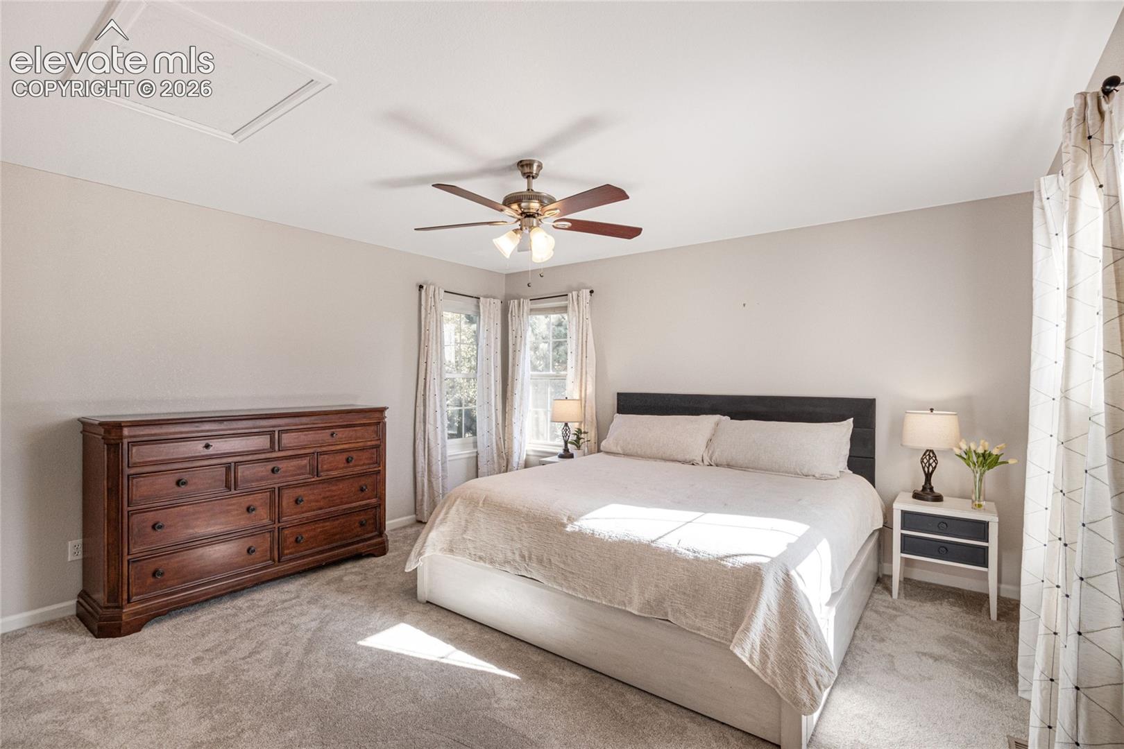 Neutral-toned room featuring neutral wall-to-wall carpeting, dual windows, and a multi-blade ceiling fan with integrated lighting