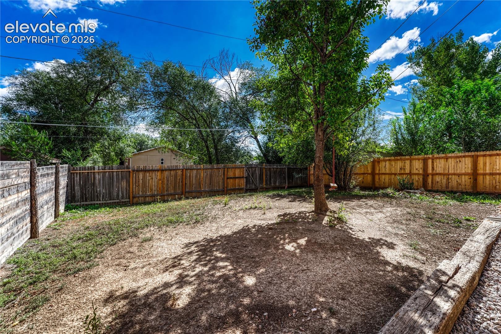 Expansive exterior space featuring a mature tree, natural ground cover, and a combination of wood fences
