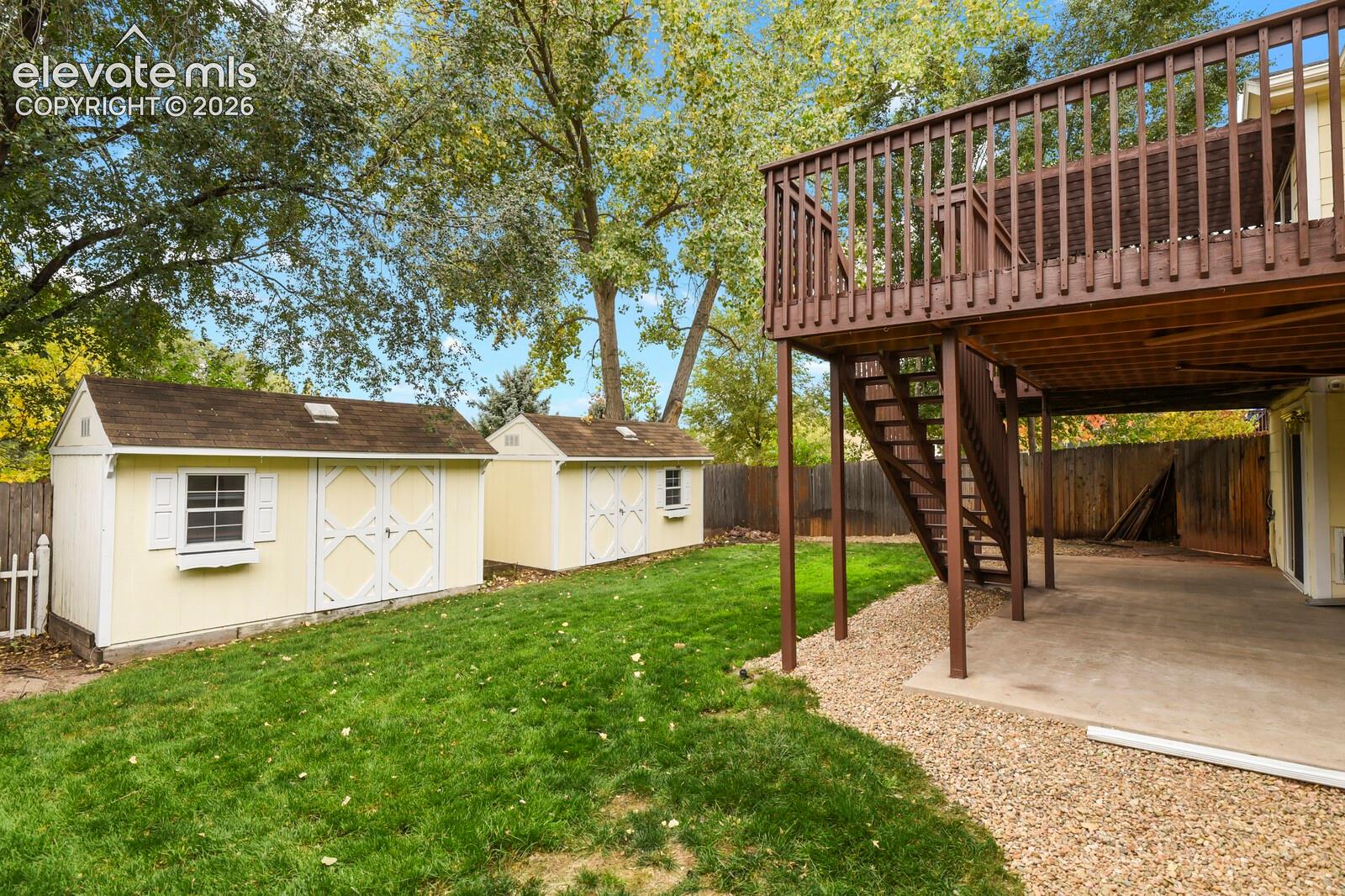 Backyard featuring two detached storage structures, a multi-level wood deck, a covered ground-level concrete patio, and a wood privacy fence