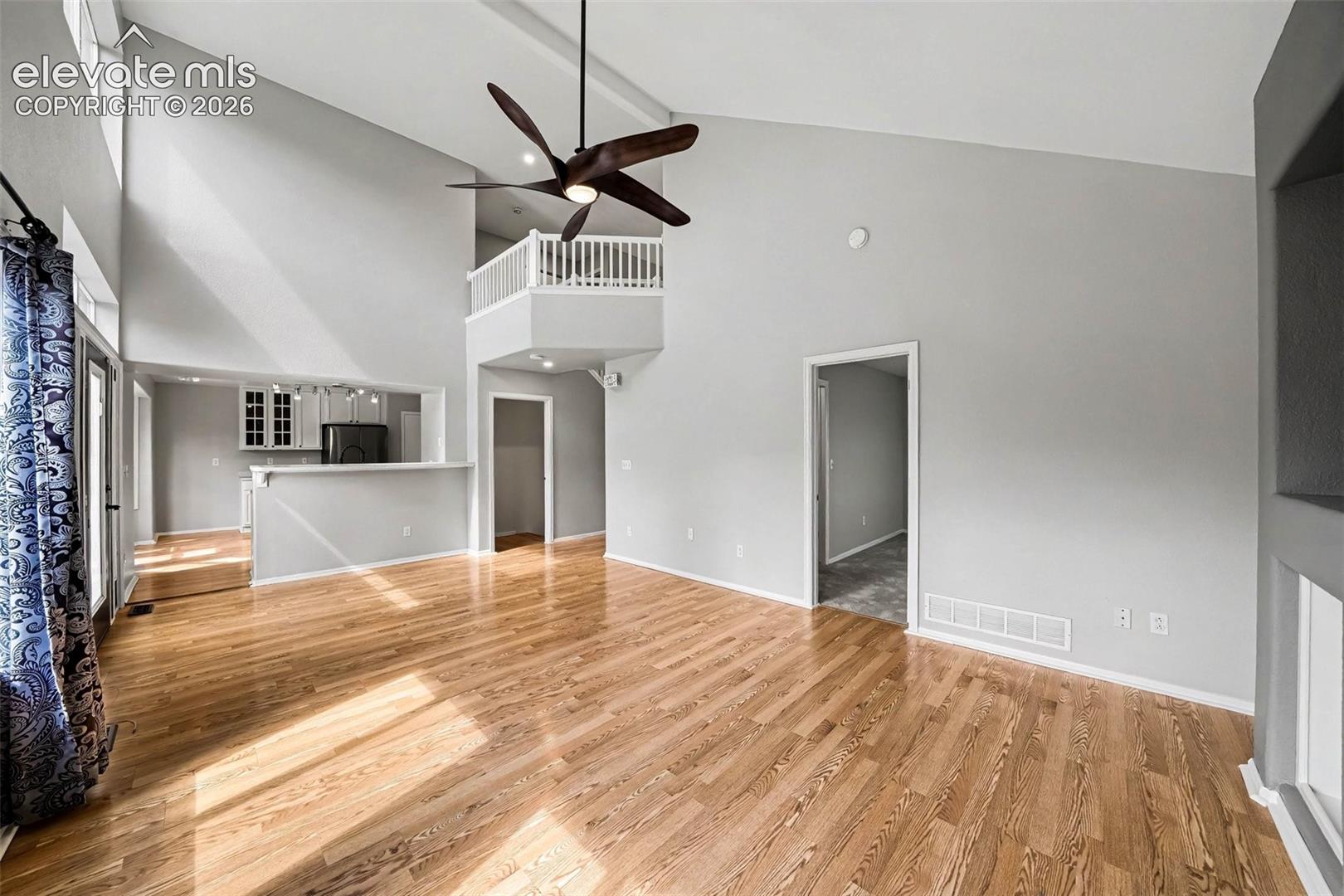 Vaulted ceiling with exposed beams, hardwood flooring, ceiling fan, and an interior balcony with white railing