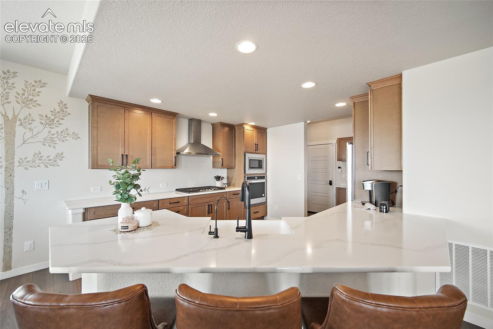 Kitchen featuring light wood cabinetry, recessed lighting, stainless steel appliances, and a large island with a built-in sink and white countertop