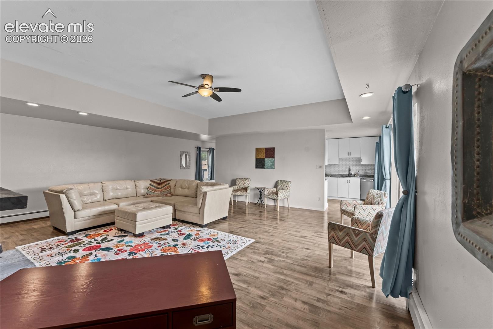 Open-concept interior featuring tray ceilings, recessed lighting, wood-finish flooring, and cabinetry with integrated hardware
