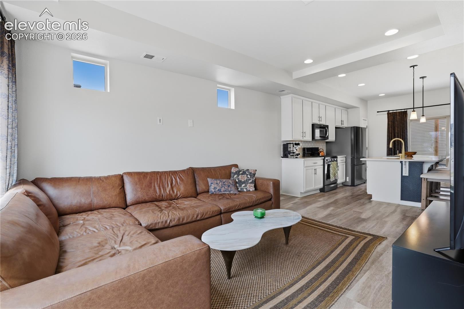 Open-concept living space featuring wood-finish flooring, recessed lighting, and a kitchen with white cabinetry