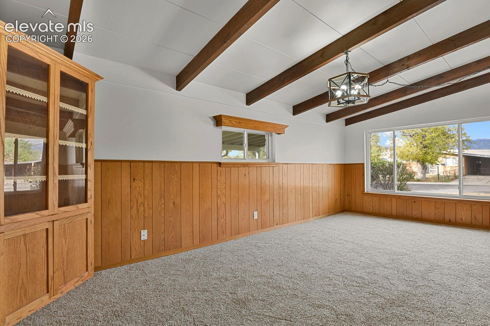 Vaulted ceiling featuring exposed wood beams, wall-to-wall wood paneling, built-in floor-to-ceiling cabinetry, and a geometric metal pendant light fixture