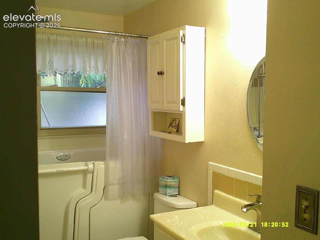 Wall-mounted medicine cabinet with open shelving, circular wall mirror, and a walk-in bathtub with a shower attachment