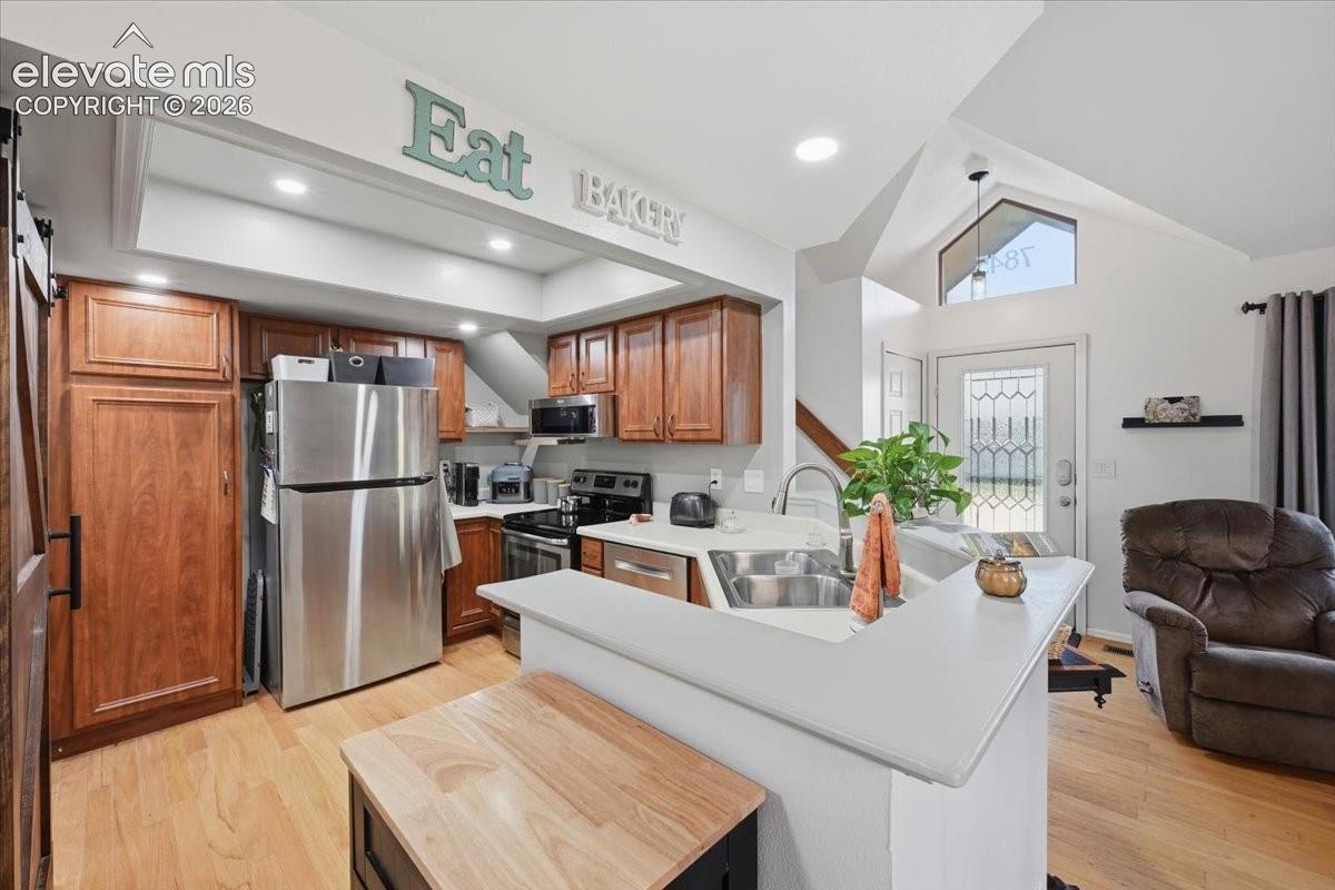 Kitchen featuring shaker-style wood cabinetry, stainless steel appliances, wood-finish flooring, vaulted ceilings, and a solid-surface peninsula countertop
