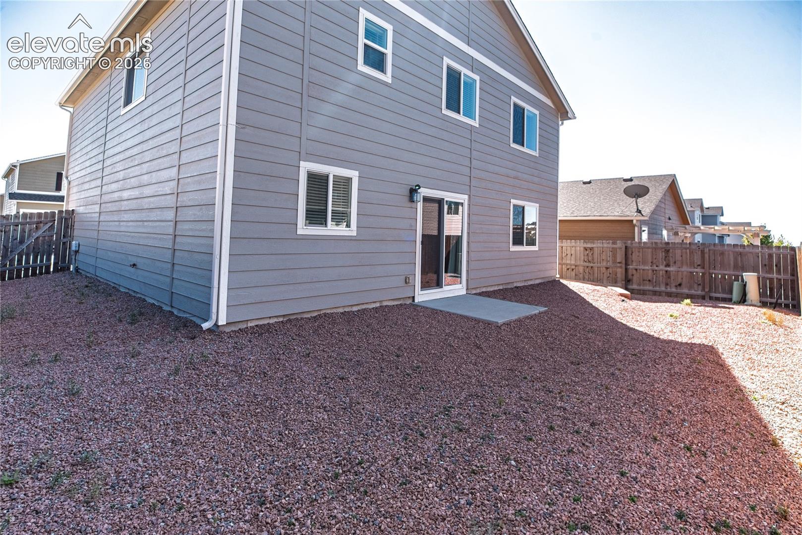 Two-story exterior with horizontal siding, multiple windows, a sliding glass door, and a concrete patio