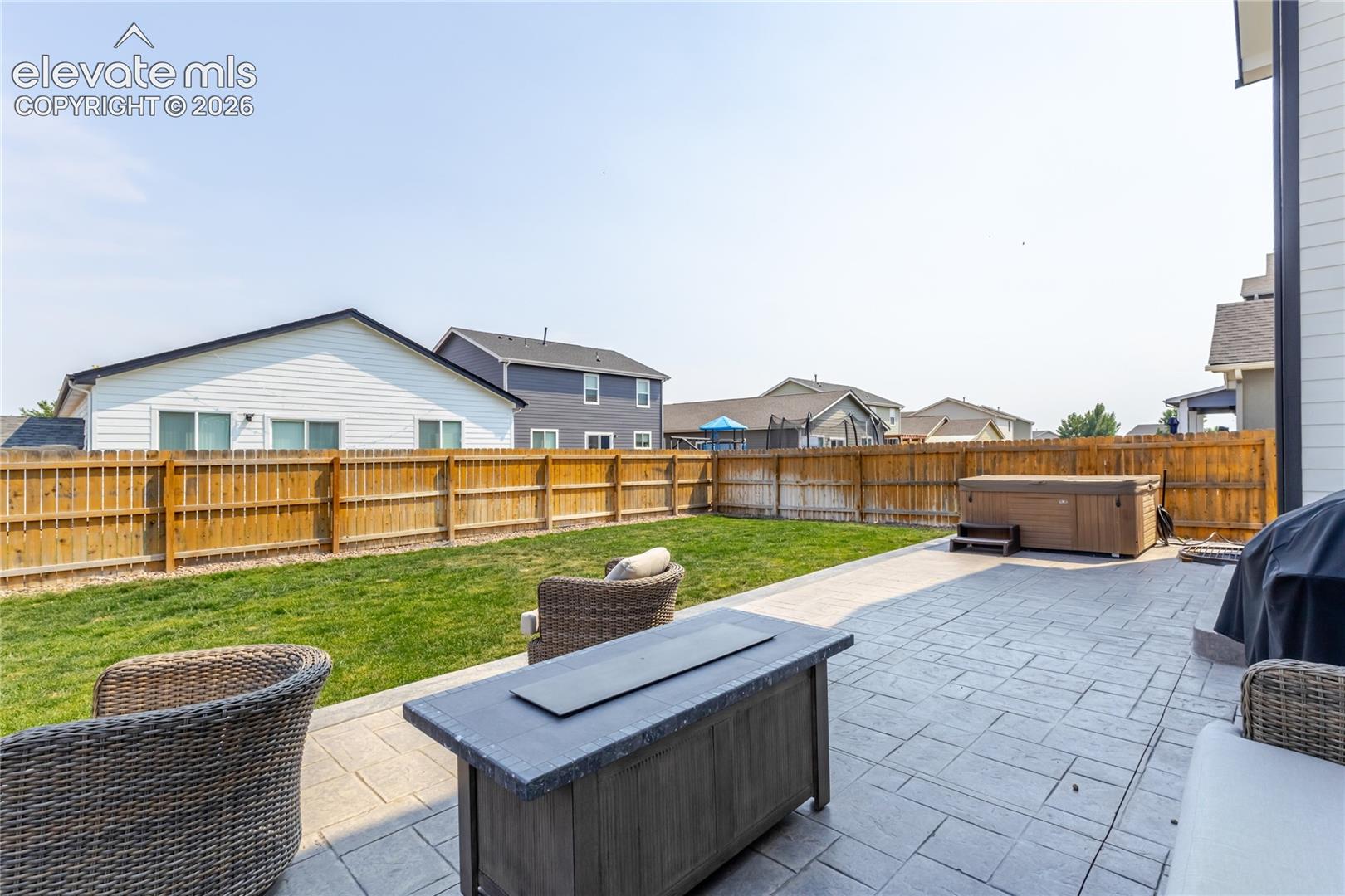 Spacious backyard featuring a stamped concrete patio, a hot tub with steps, and a grassy lawn enclosed by a wood privacy fence