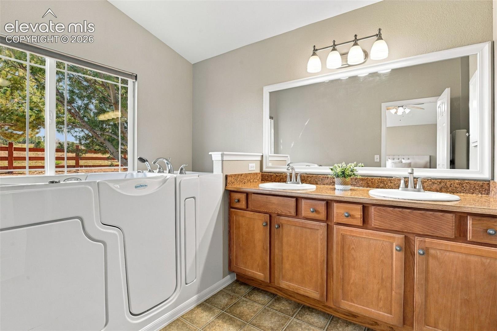 Walk-in tub with window, double vanity with stone-finish countertop, and integrated sinks