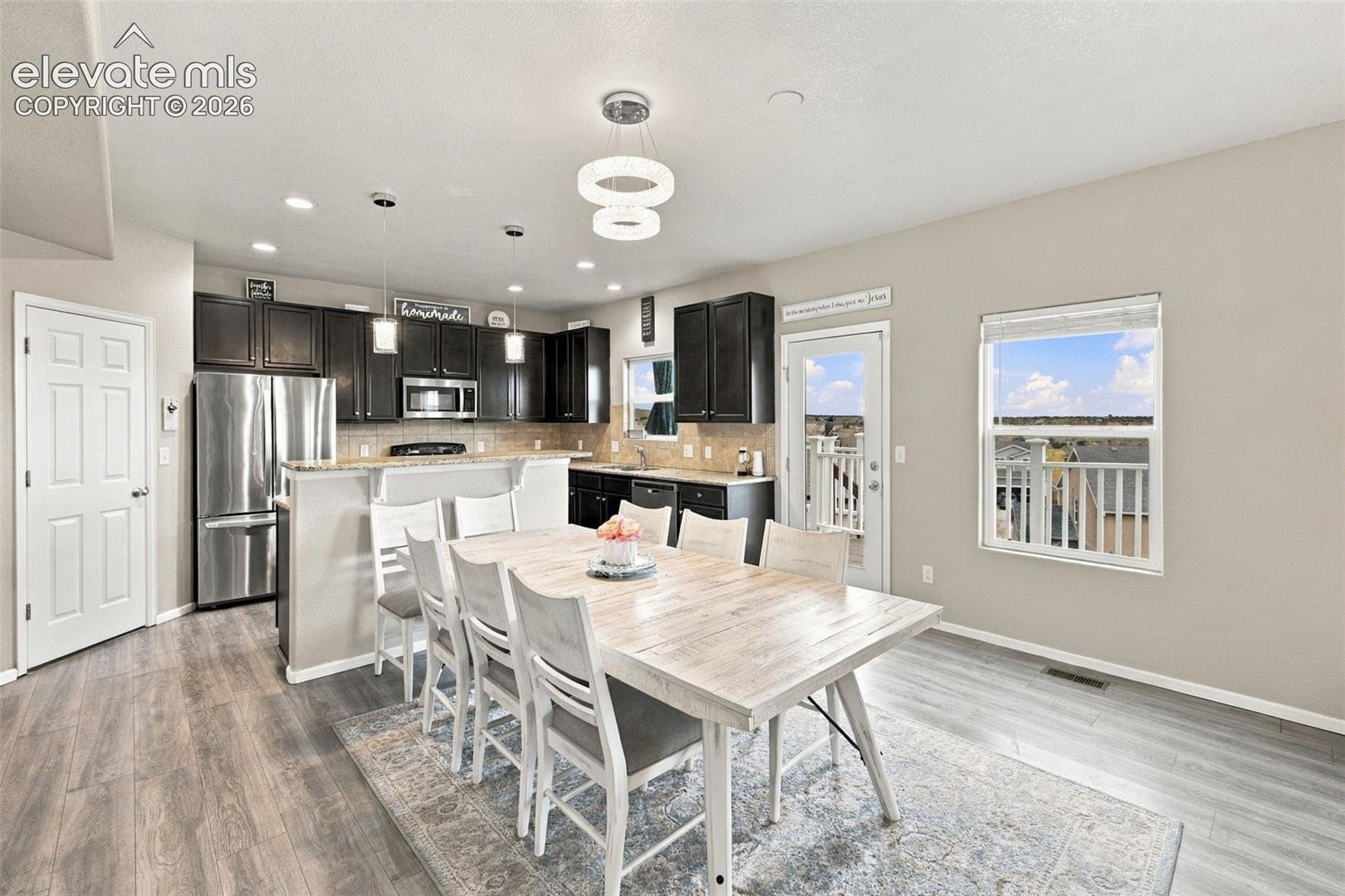 Kitchen featuring dark cabinetry, stone-finish countertops, stainless steel appliances, modern circular pendant lighting, and wood-finish flooring