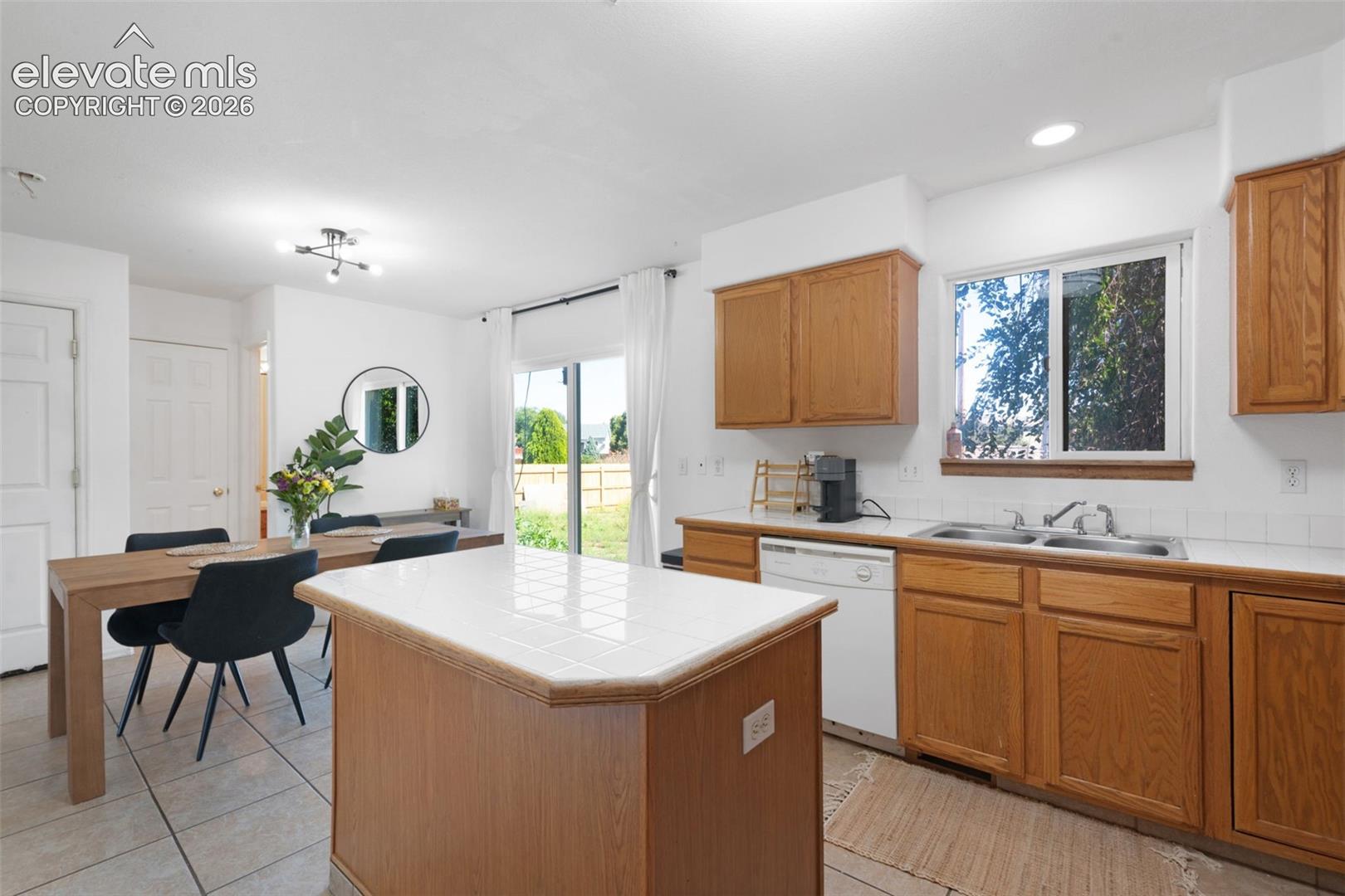 Open-concept kitchen featuring wood-finish cabinetry, tile countertops, a built-in dishwasher, and an island with a tile surface