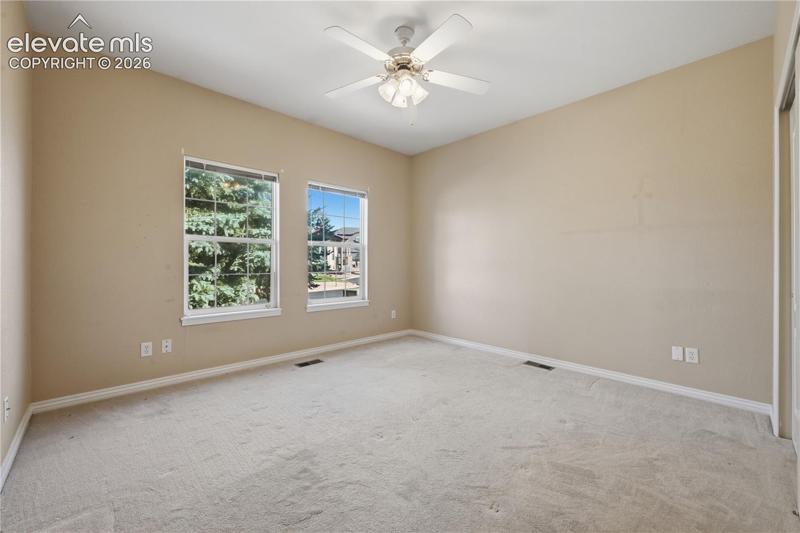 Neutral-toned room featuring wall-to-wall carpeting, dual windows, and a ceiling-mounted light fixture with integrated fan
