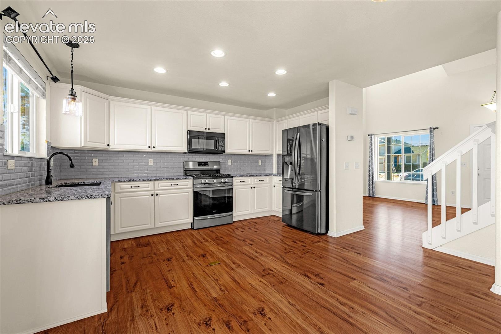 Kitchen featuring white cabinetry, stone-finish countertops, subway tile backsplash, stainless steel appliances, and wood-finish flooring