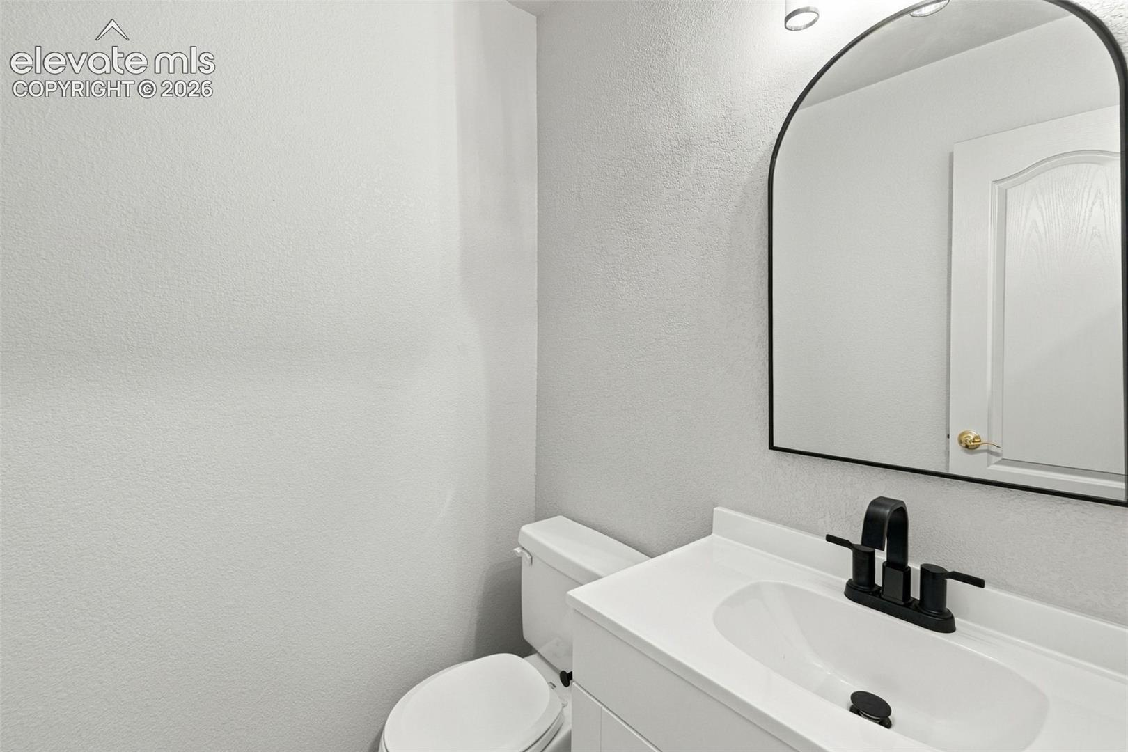 White vanity with an integrated countertop, arched mirror with a thin black frame, and matte black two-handle faucet