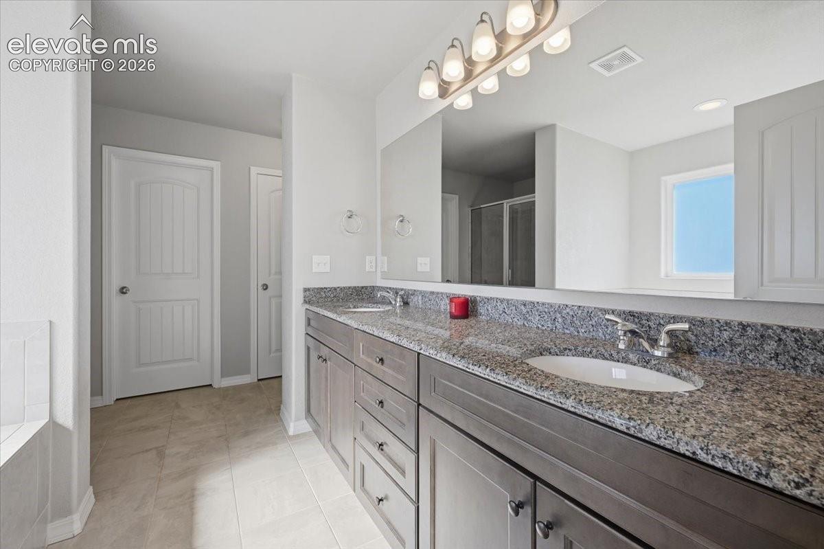 Dual-sink vanity with stone-finish countertops, undermount sinks, custom cabinetry, large-format mirror, and multi-bulb light fixture