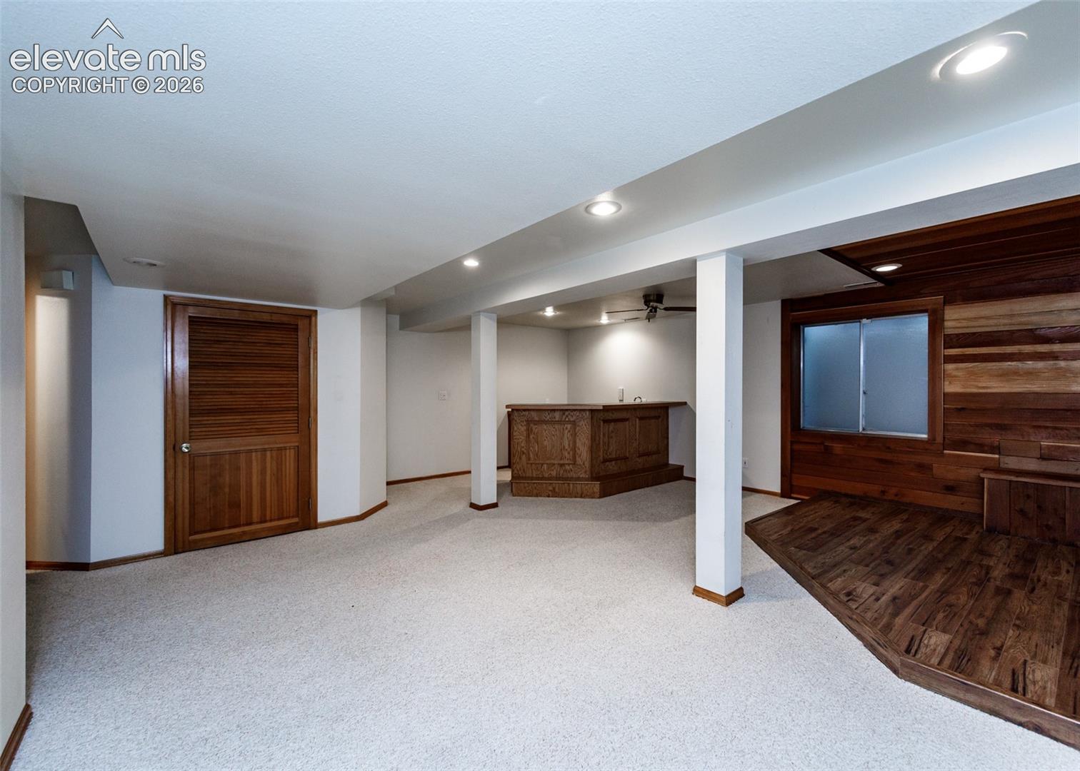 Finished lower level featuring recessed lighting, a built-in wet bar, wood-finish flooring, and a paneled accent wall