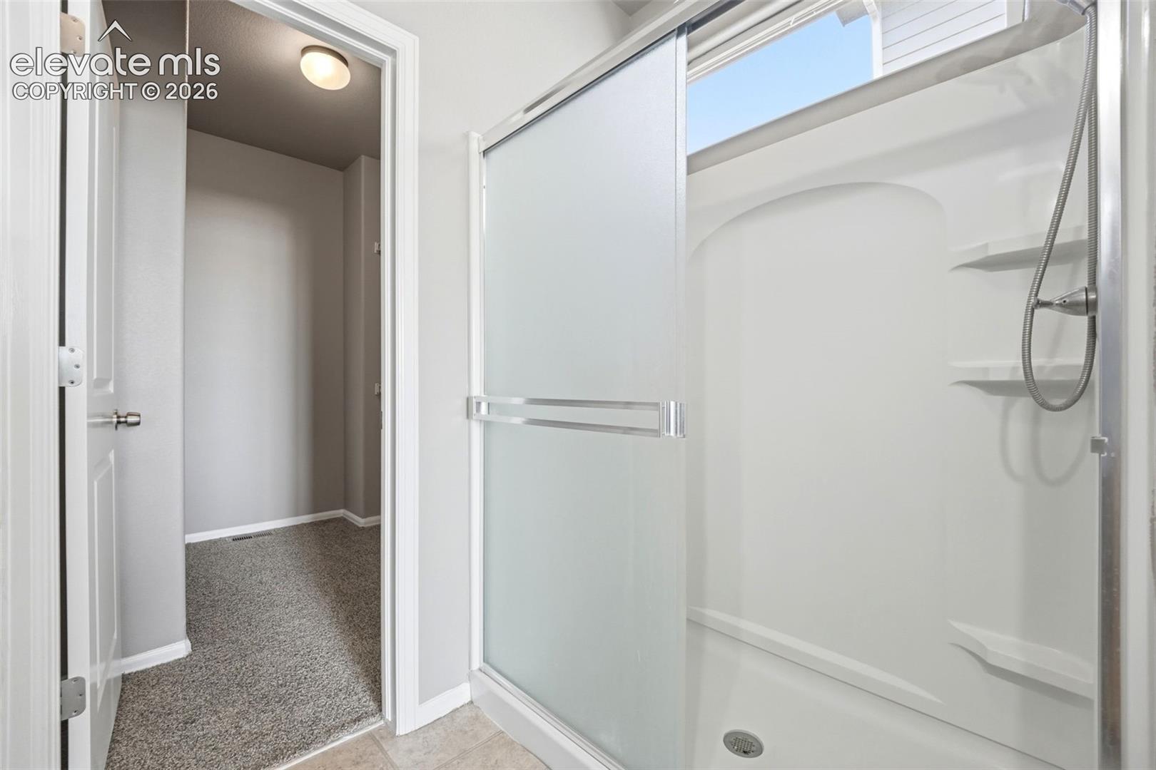 Shower with a sliding frosted glass door, integrated shelving, and a chrome-finish shower head