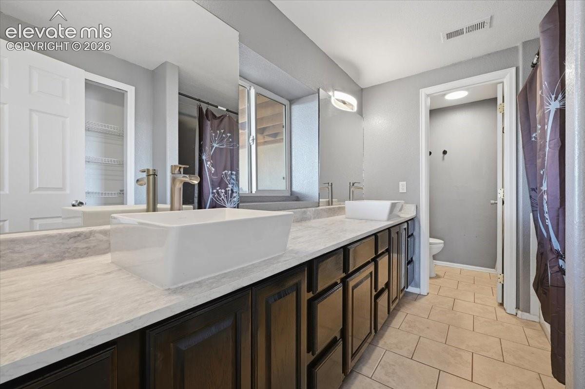 Dual-sink vanity featuring rectangular vessel basins, stone-patterned countertops, dark wood-finish cabinetry, and brushed metallic fixtures