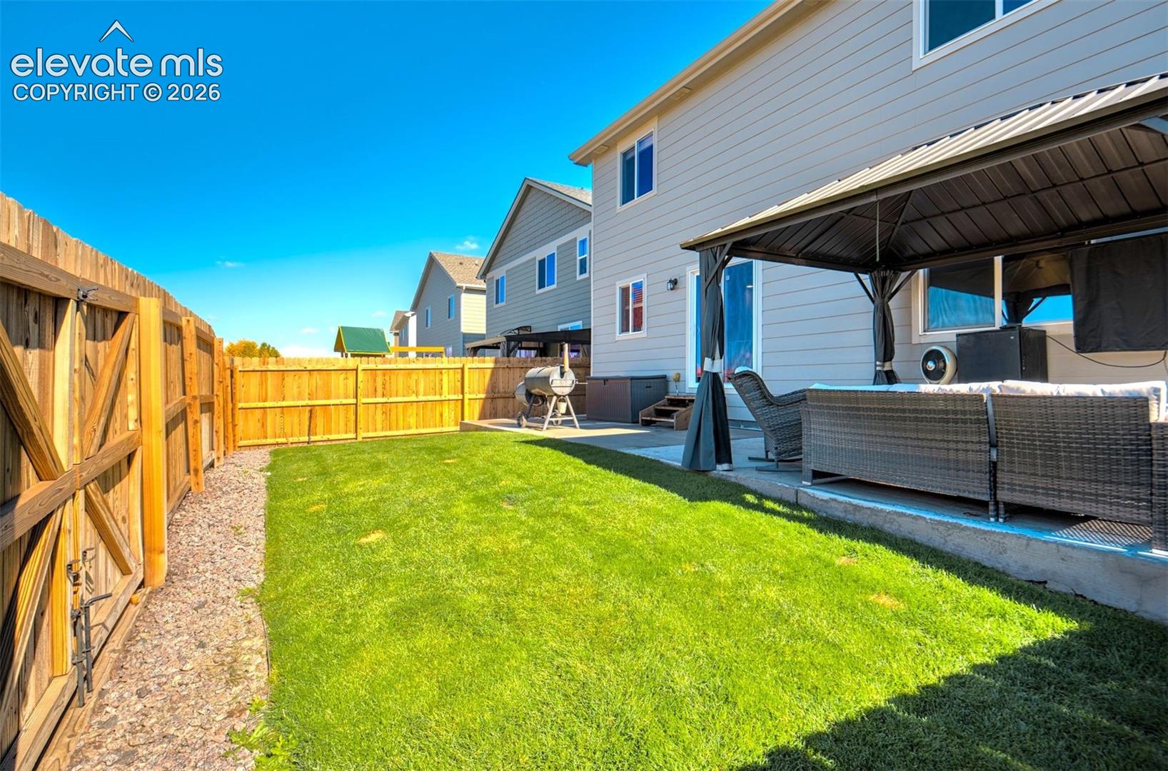 Fenced backyard featuring a manicured lawn, concrete patio, and structural gazebo