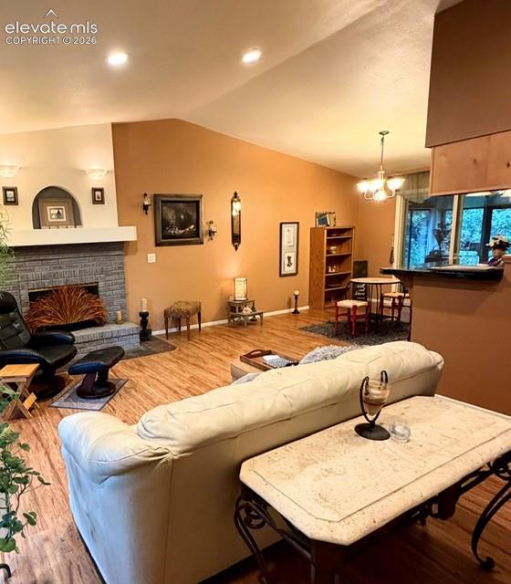 Living area featuring vaulted ceilings, wood-finish flooring, a stone-faced fireplace with a mantel, recessed lighting, and an open concept layout