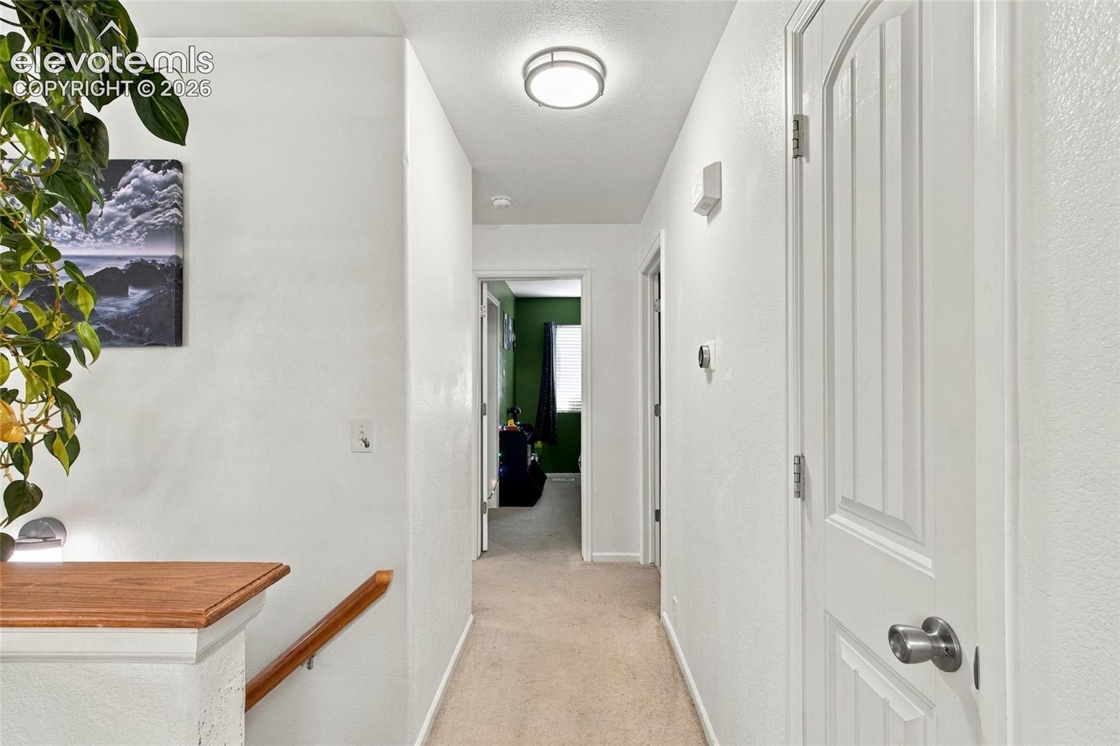 Hallway to bedrooms and laundry featuring neutral carpeting, and a wood finish stair railing