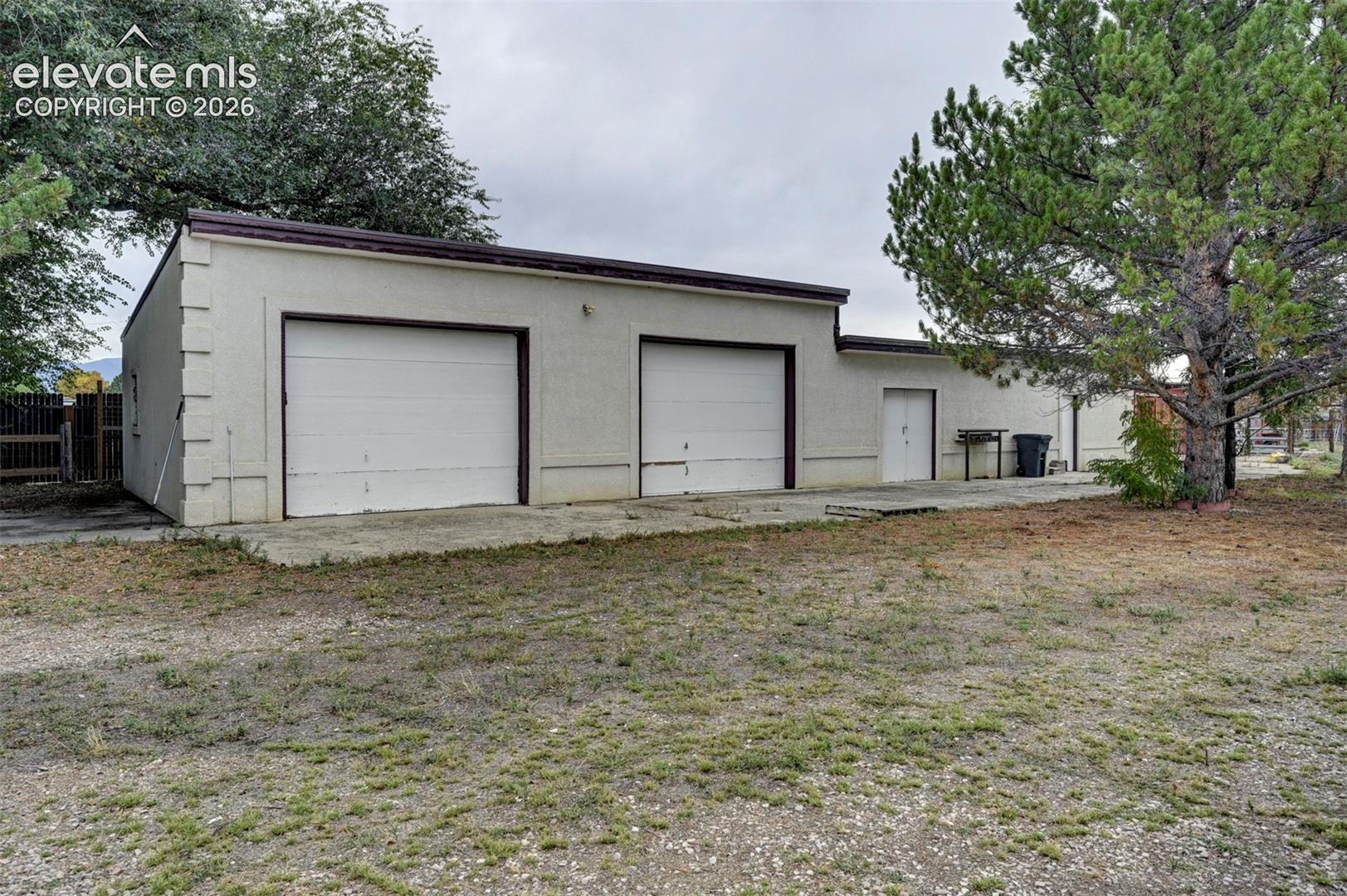Stucco exterior structure featuring two garage doors and a separate entry door