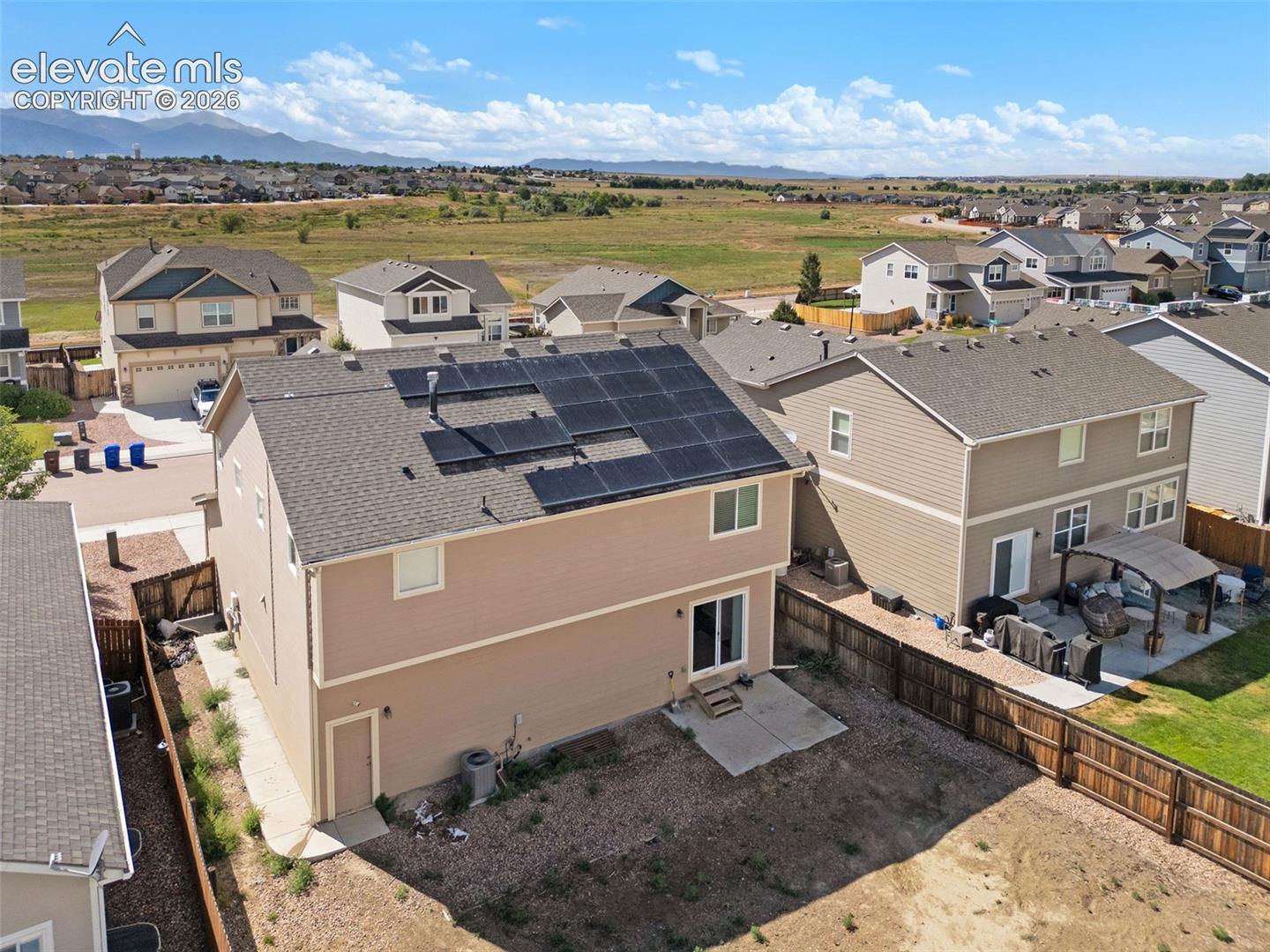 Two-story residence featuring asphalt shingle roofing, integrated rooftop solar panels, a concrete rear patio, and a wood privacy fence