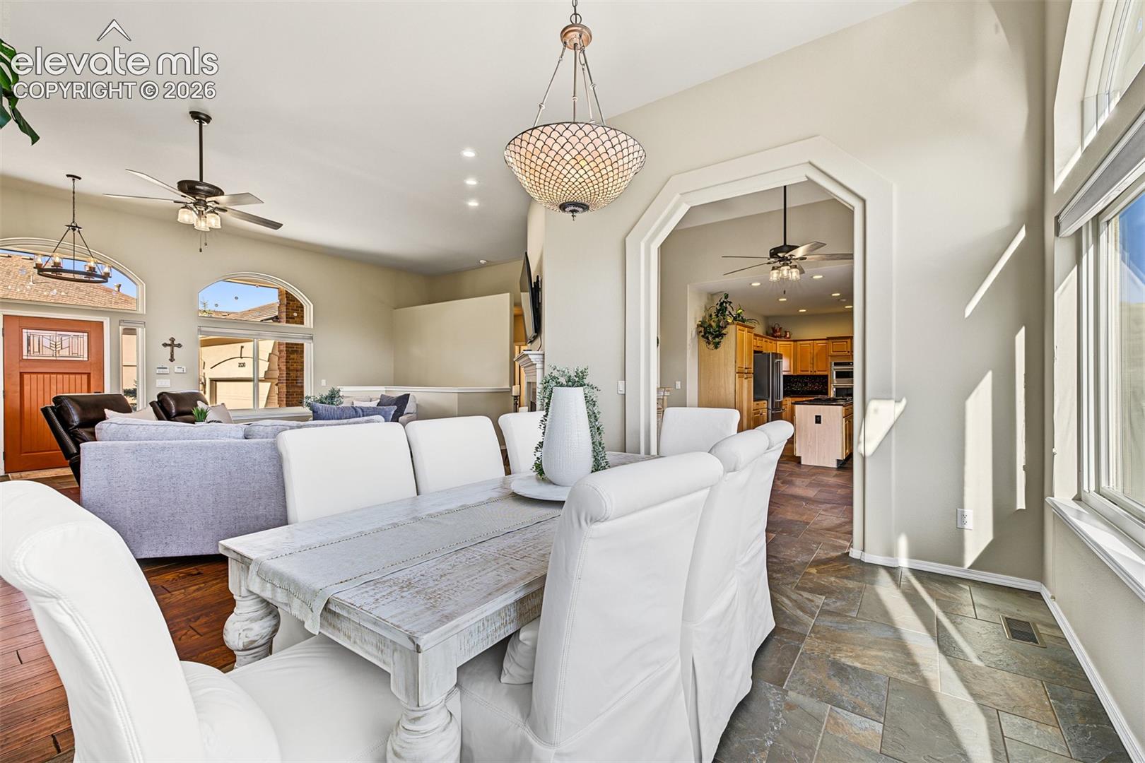 Light-filled dining area featuring a statement chandelier, tile flooring, and large windows offering mountain views and overlooking the rear deck. Open to the living room and kitchen.
