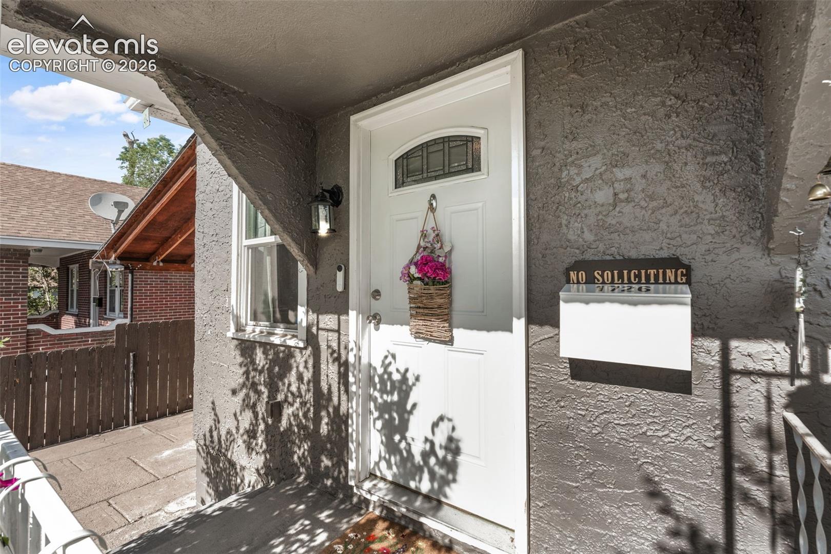 Front entry featuring a white paneled door with an arched glass insert, textured exterior wall finish, and an exterior wall lantern