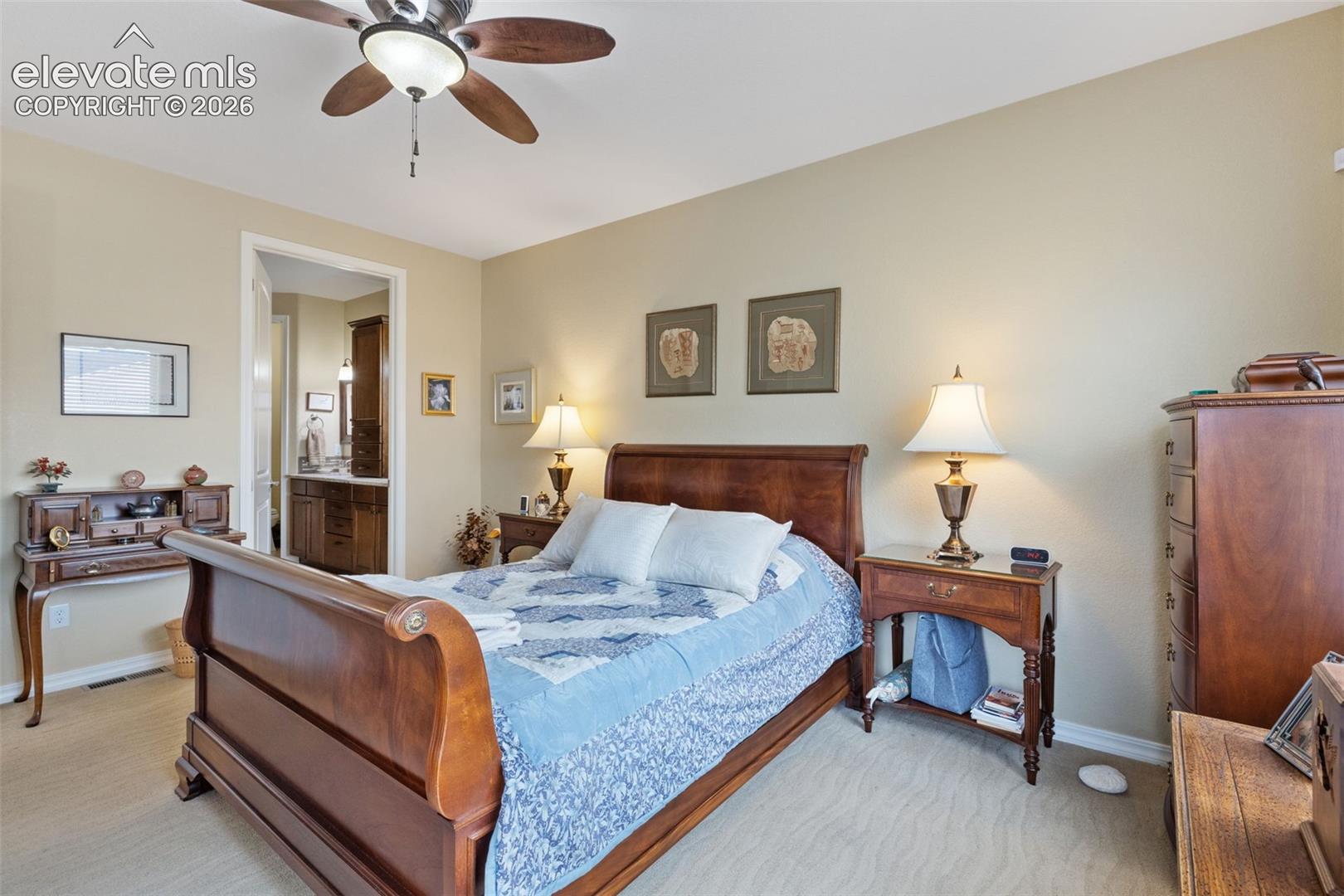 Carpeted master bedroom with a ceiling fan, recessed lighting, and an entryway to a bathroom featuring a wood-finish vanity with a countertop