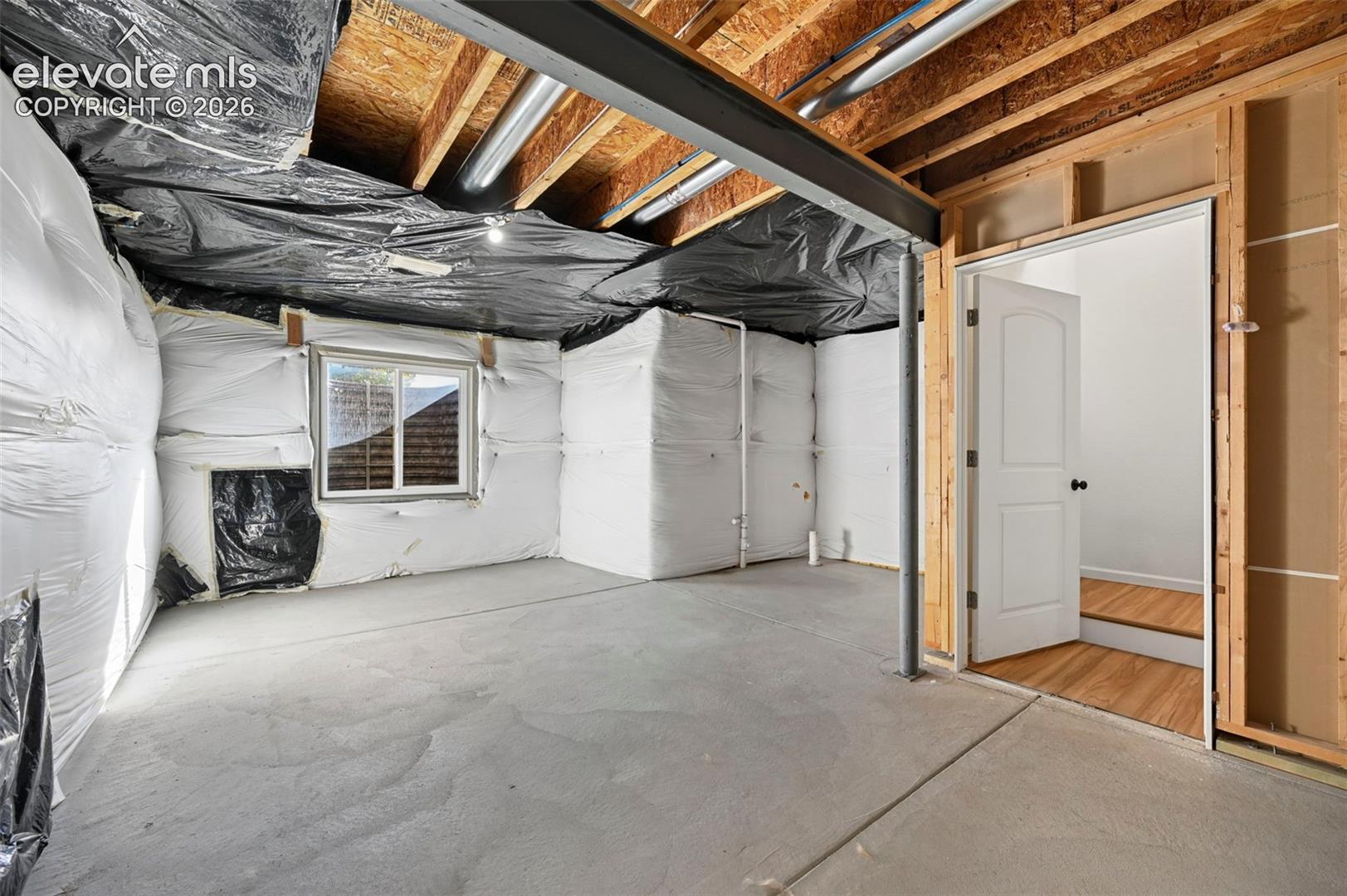 Unfinished basement area featuring exposed ceiling joists, concrete flooring, perimeter insulation, a single window, and structural steel support columns