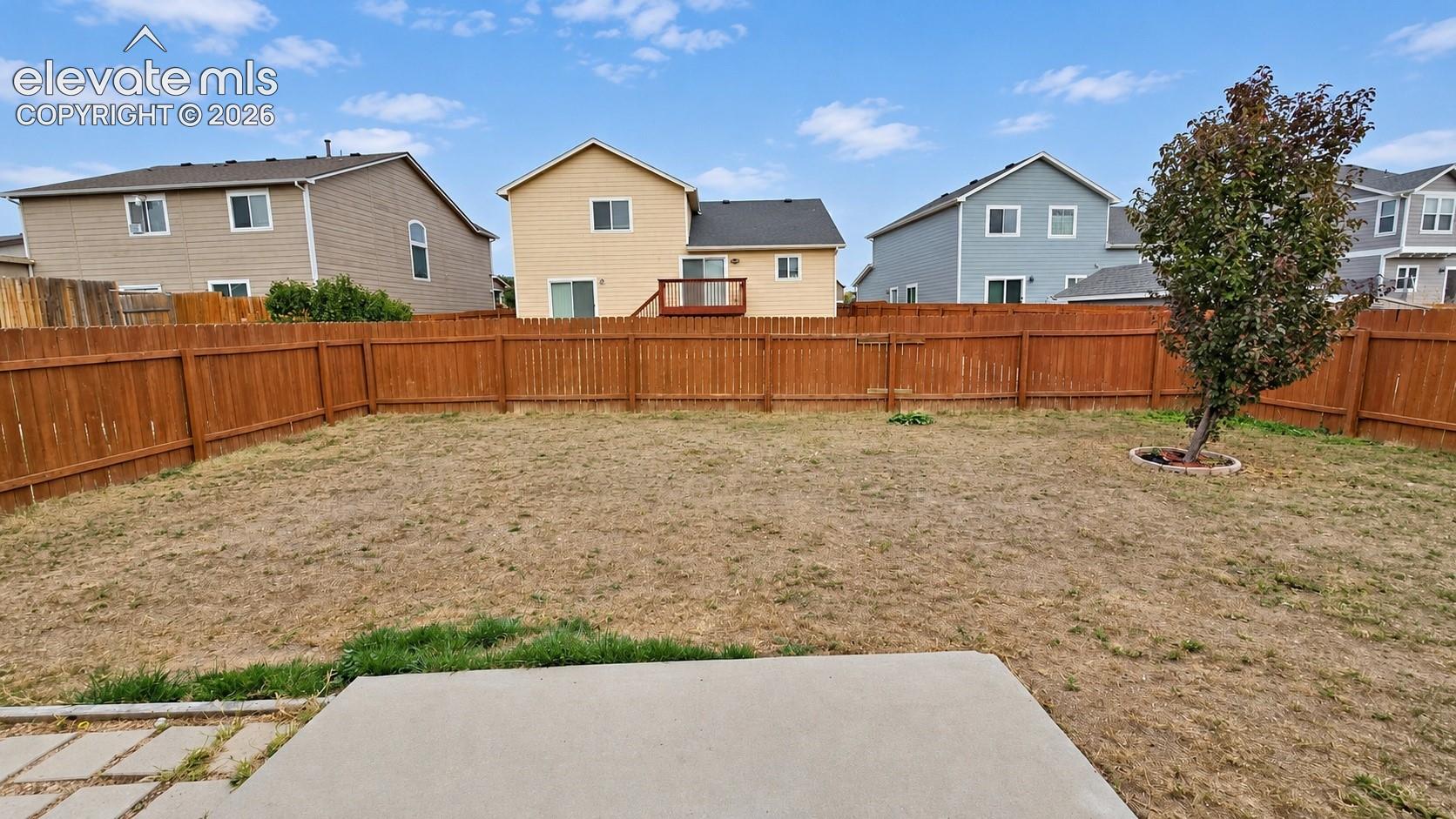 Backyard featuring a wood privacy fence, concrete patio, and a mature tree