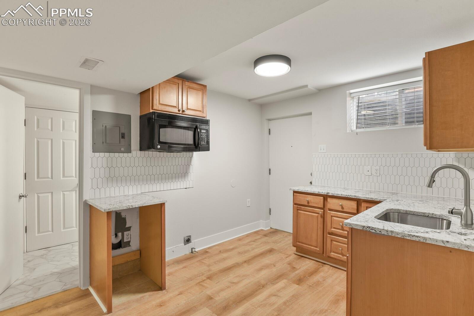 Kitchenette in basement featuring LVP flooring, microwave, sink, dishwasher hook up as well as electrical for the stove, many cabinets and private entry from the backyard.