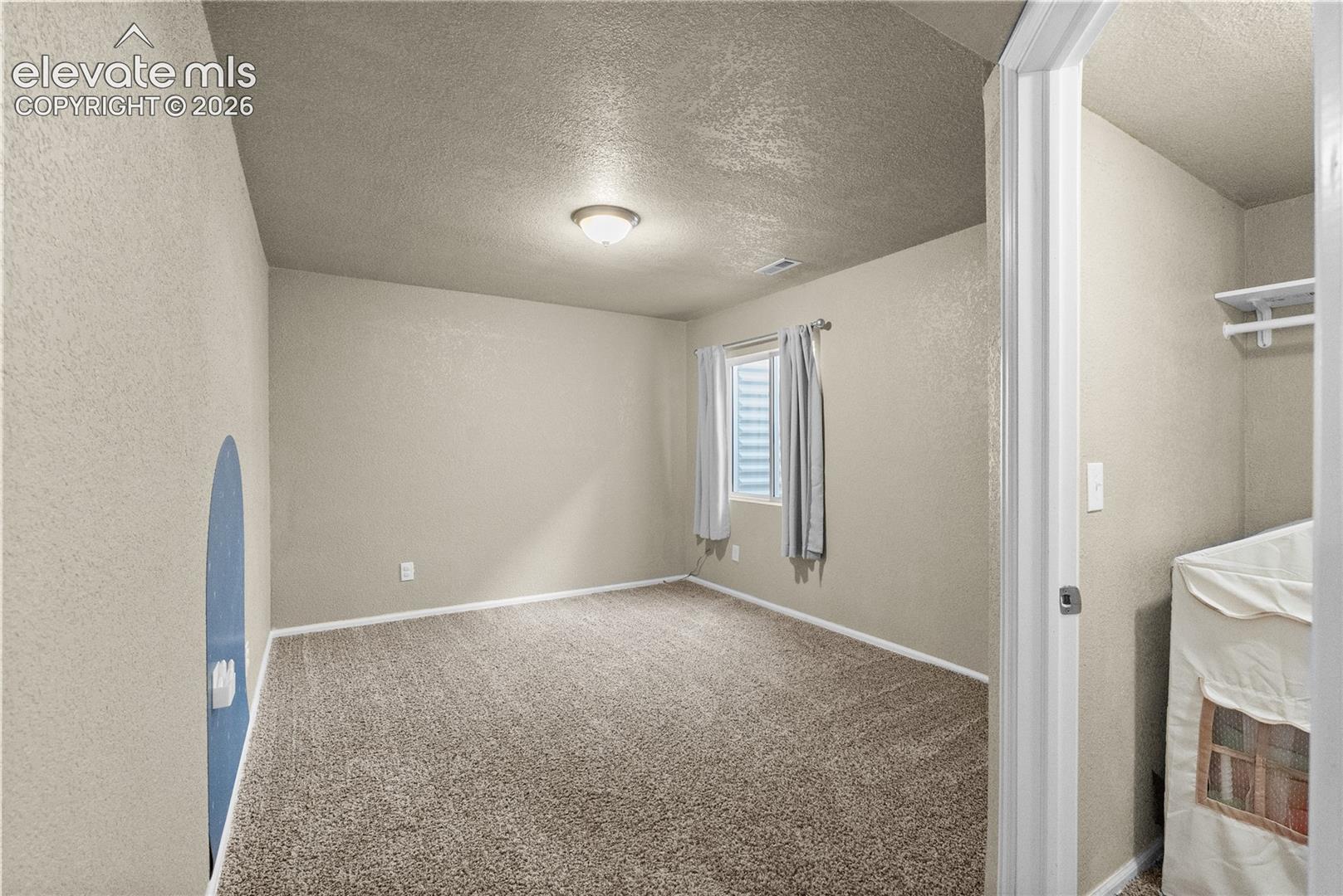 Neutral-toned wall finishes, carpeted flooring, a window with blinds, and an overhead light fixture