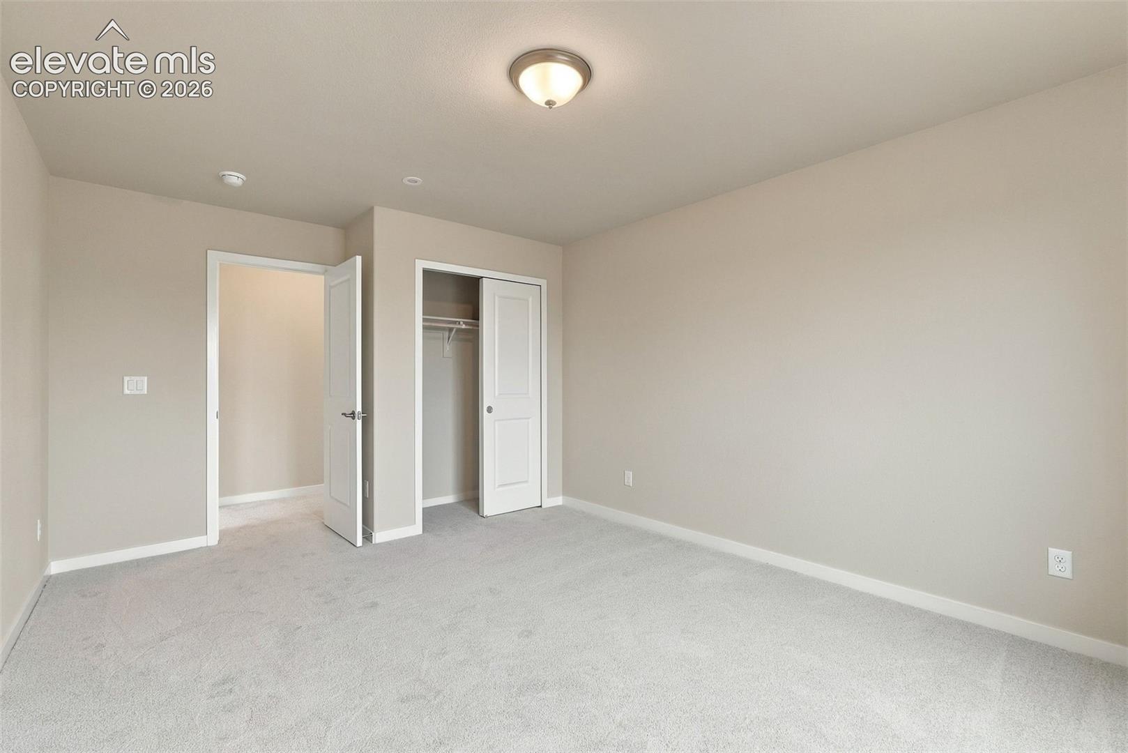 Neutral-toned room featuring wall-to-wall carpeting, a flush-mount ceiling light, and a built-in closet with panel doors