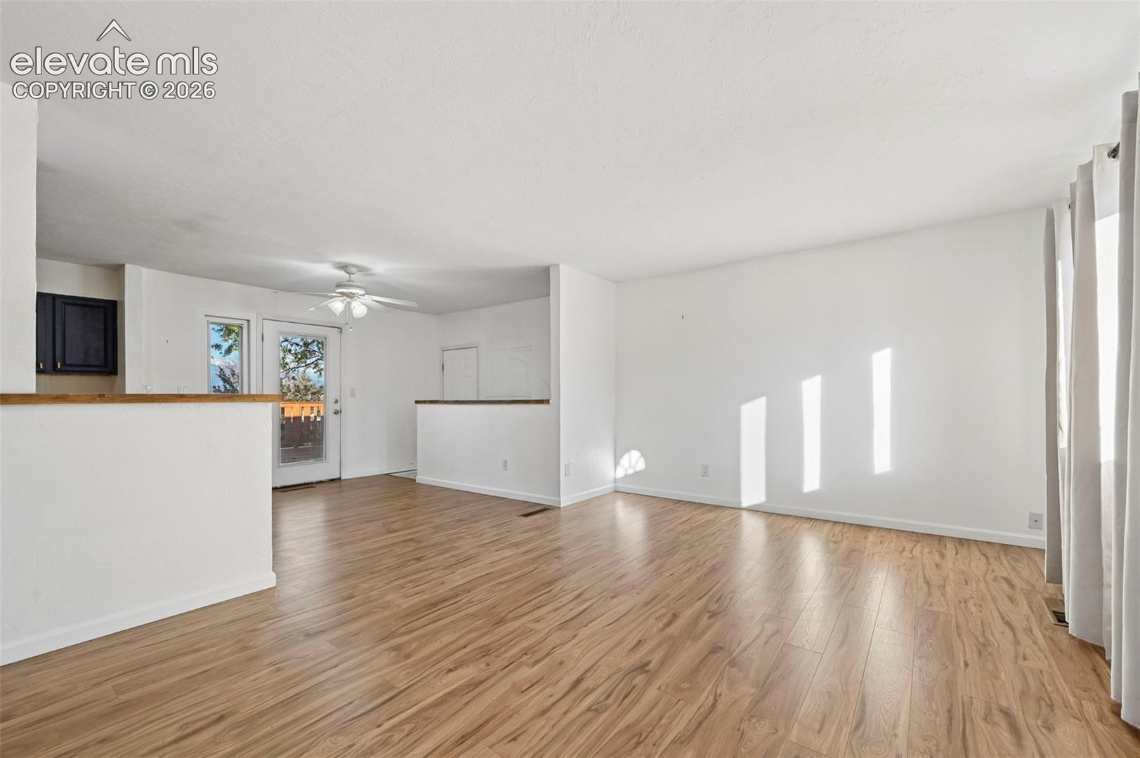 Unstaged Living area featuring wood-finish flooring, half-height room partitions with wood capping, and a ceiling fan with integrated lighting