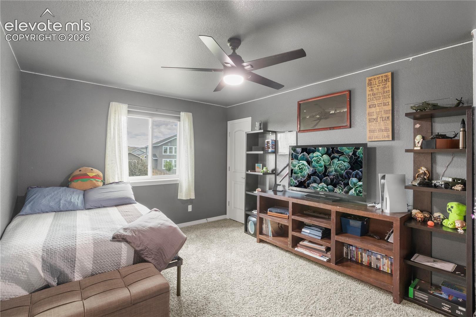 Gray walls with white trim, a large window, a ceiling fan with light fixture, and carpeted flooring