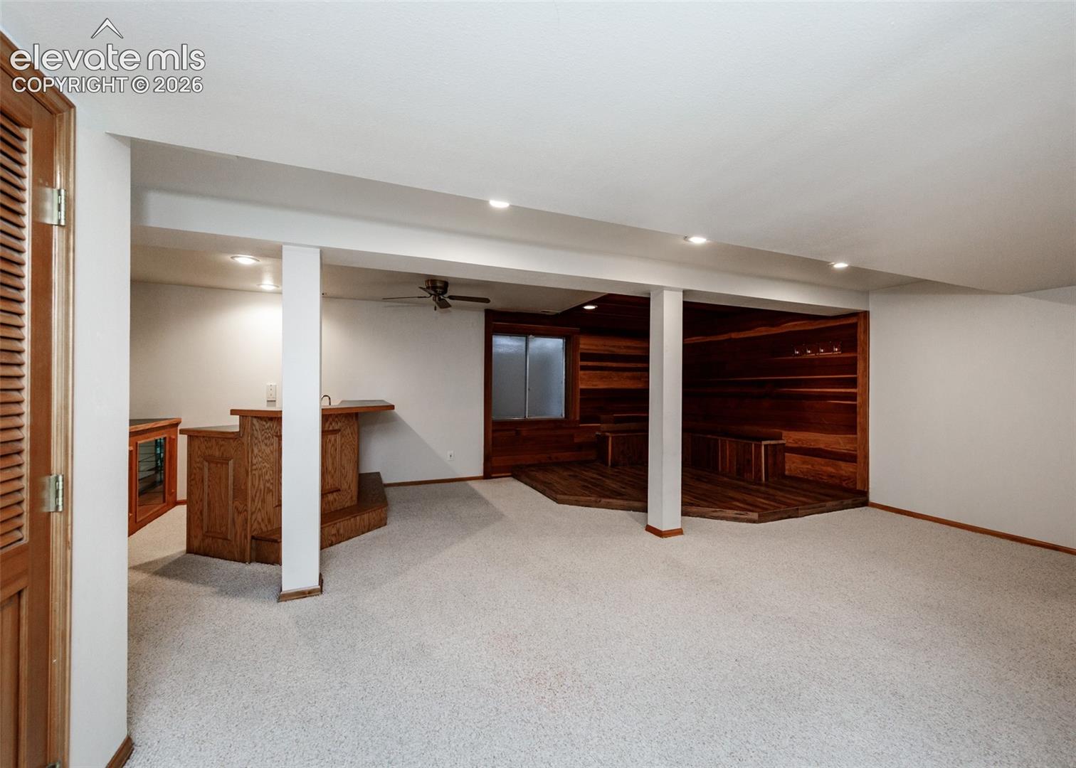 Recessed lighting throughout, wood-finish bar with built-in sink, wood-paneled wall, wood-finish flooring, and light-toned carpeting