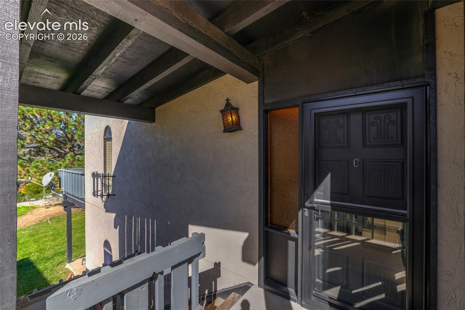 Covered entryway featuring an exposed beam ceiling, decorative metal wall-mounted lantern, and black paneled door with sidelight
