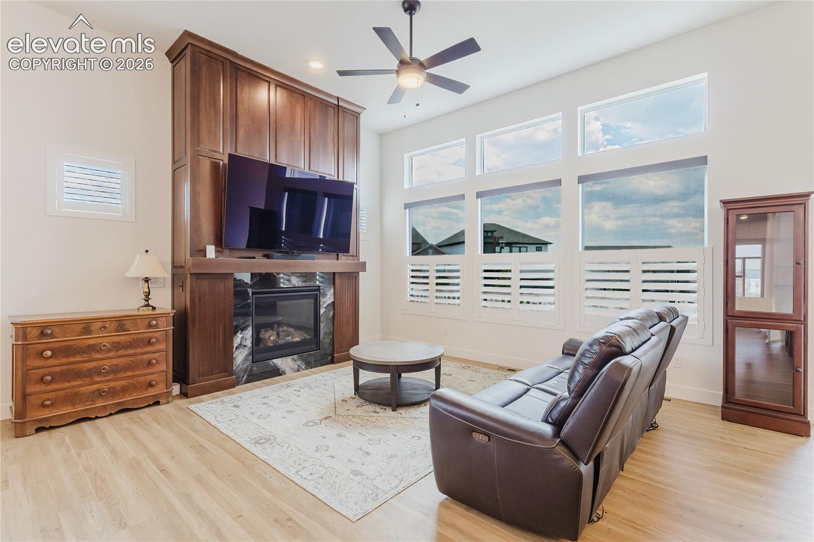 High ceilings featuring a ceiling fan, a fireplace with custim designed and built hardwood surround, and multiple windows with views of the front range and plantation shutters