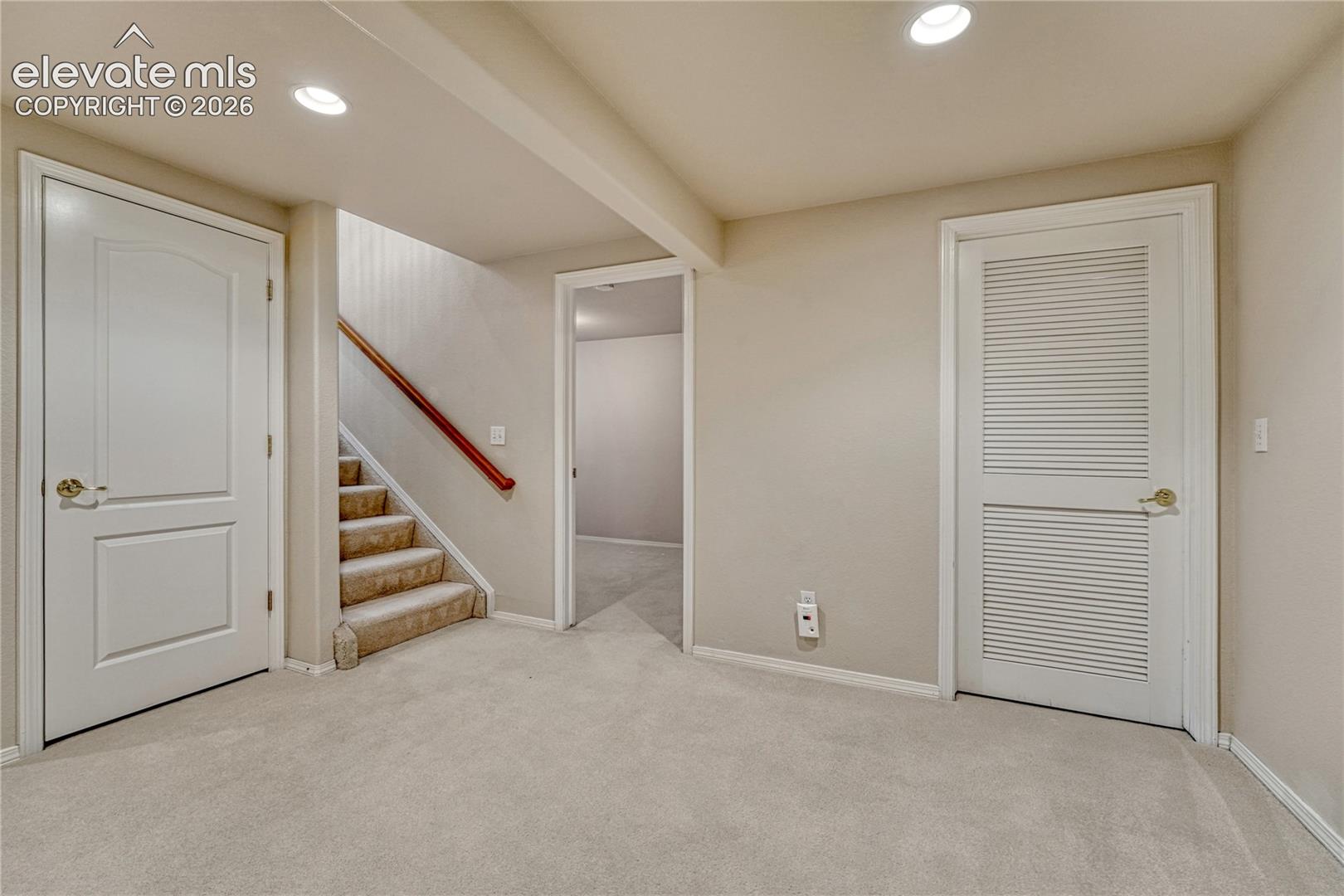 The lower-level stair landing opens to 8-foot ceilings, plush carpeting, recessed lighting, and dedicated storage doors
