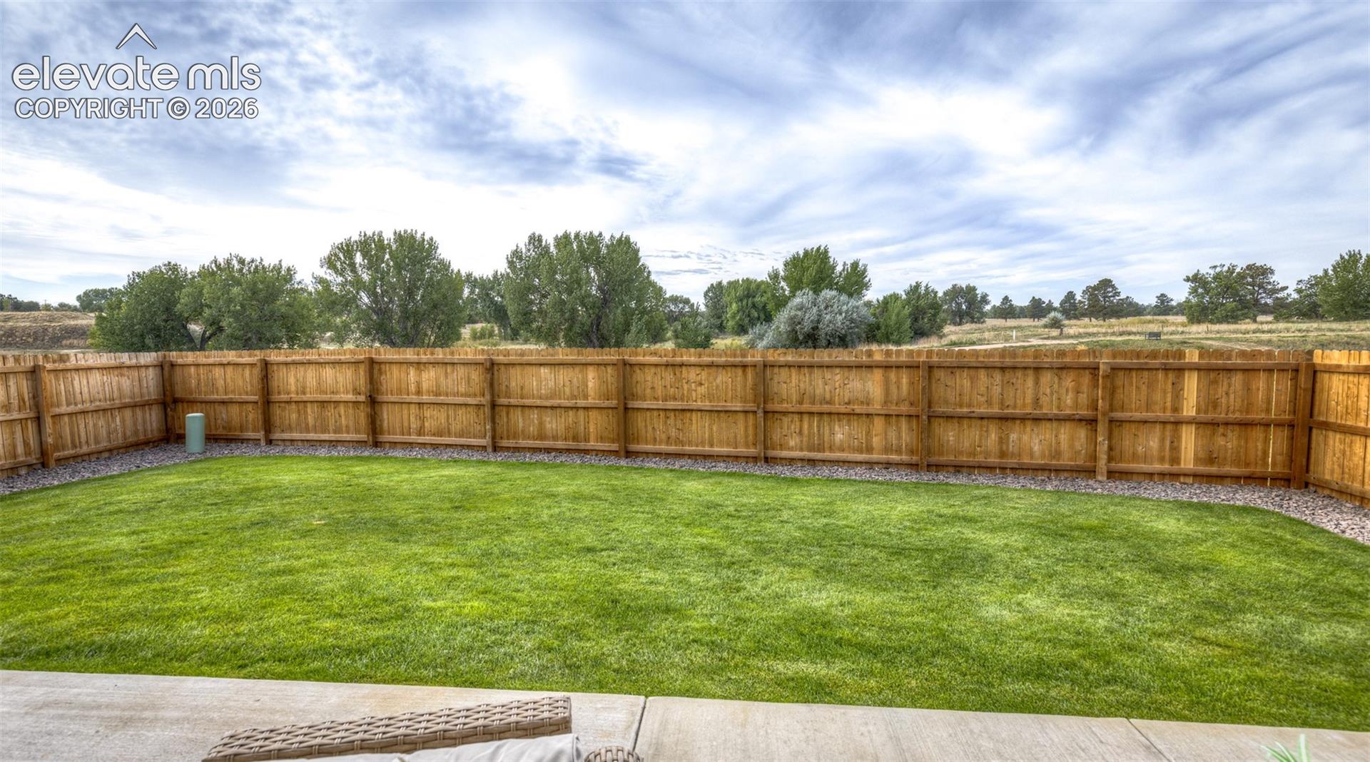 Fenced backyard featuring a manicured lawn, concrete patio, and stone border detailing