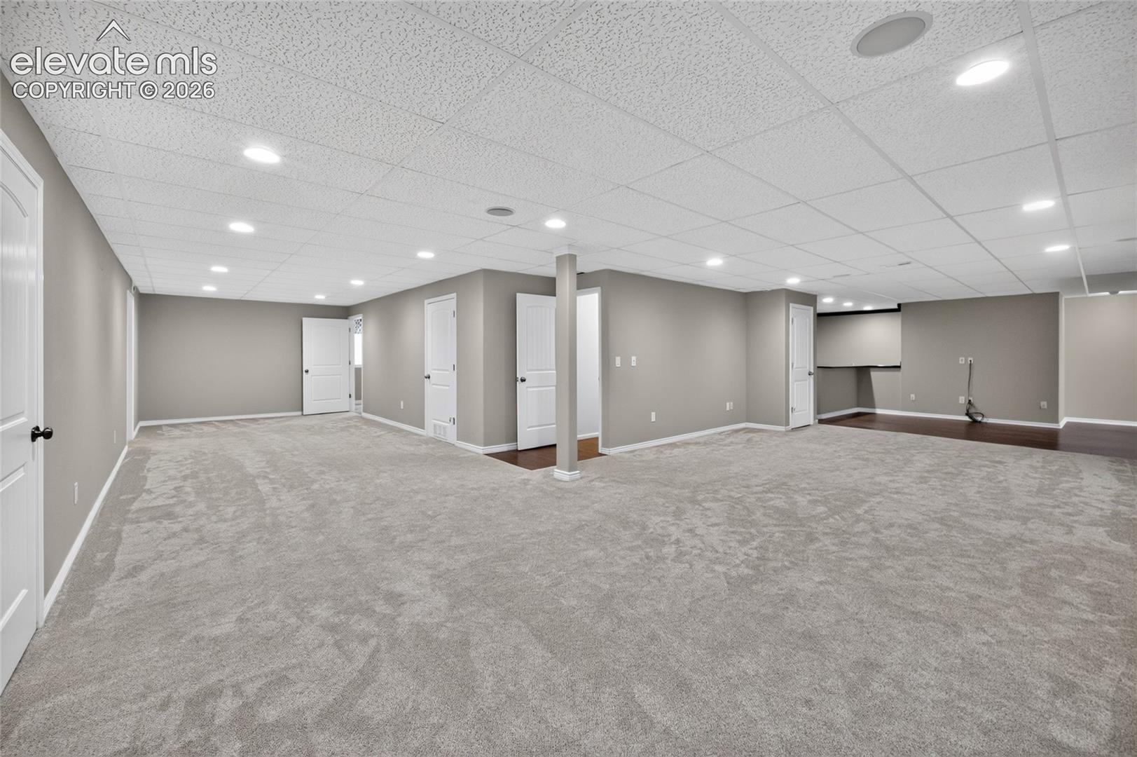 Finished lower level featuring recessed lighting, neutral carpeting, a drop ceiling, and multiple interior doors
