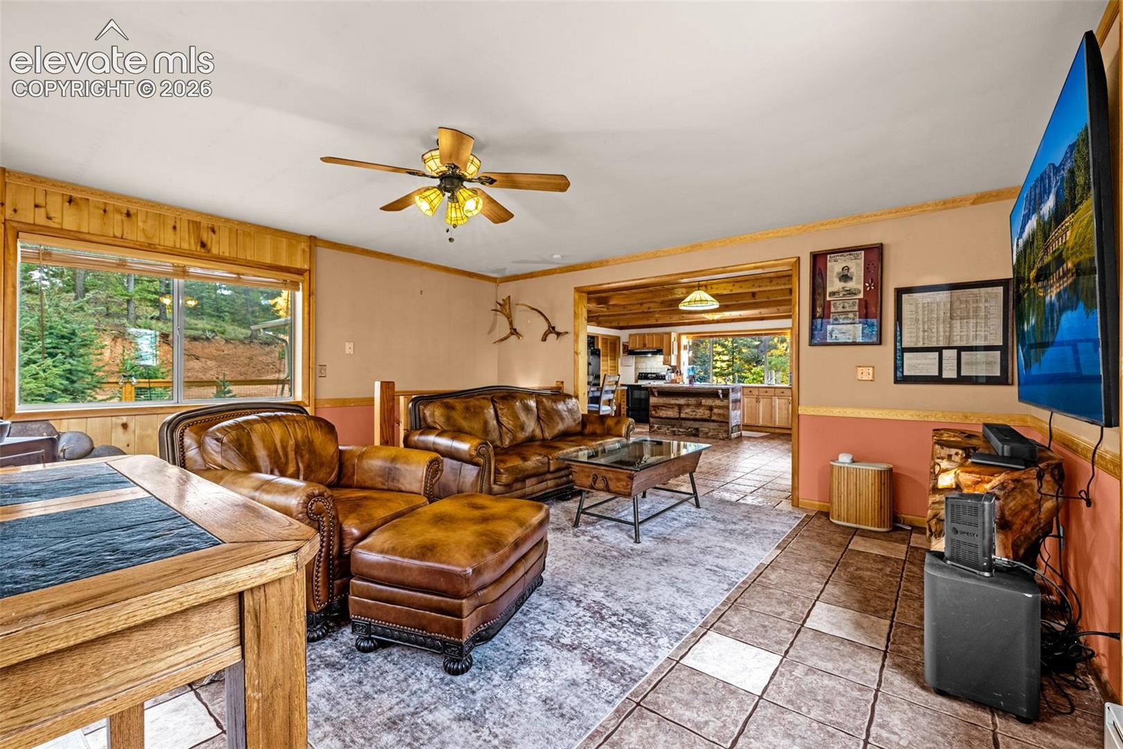 Living area featuring wood-paneled wall accents, tile flooring, and a ceiling fan with integrated lighting