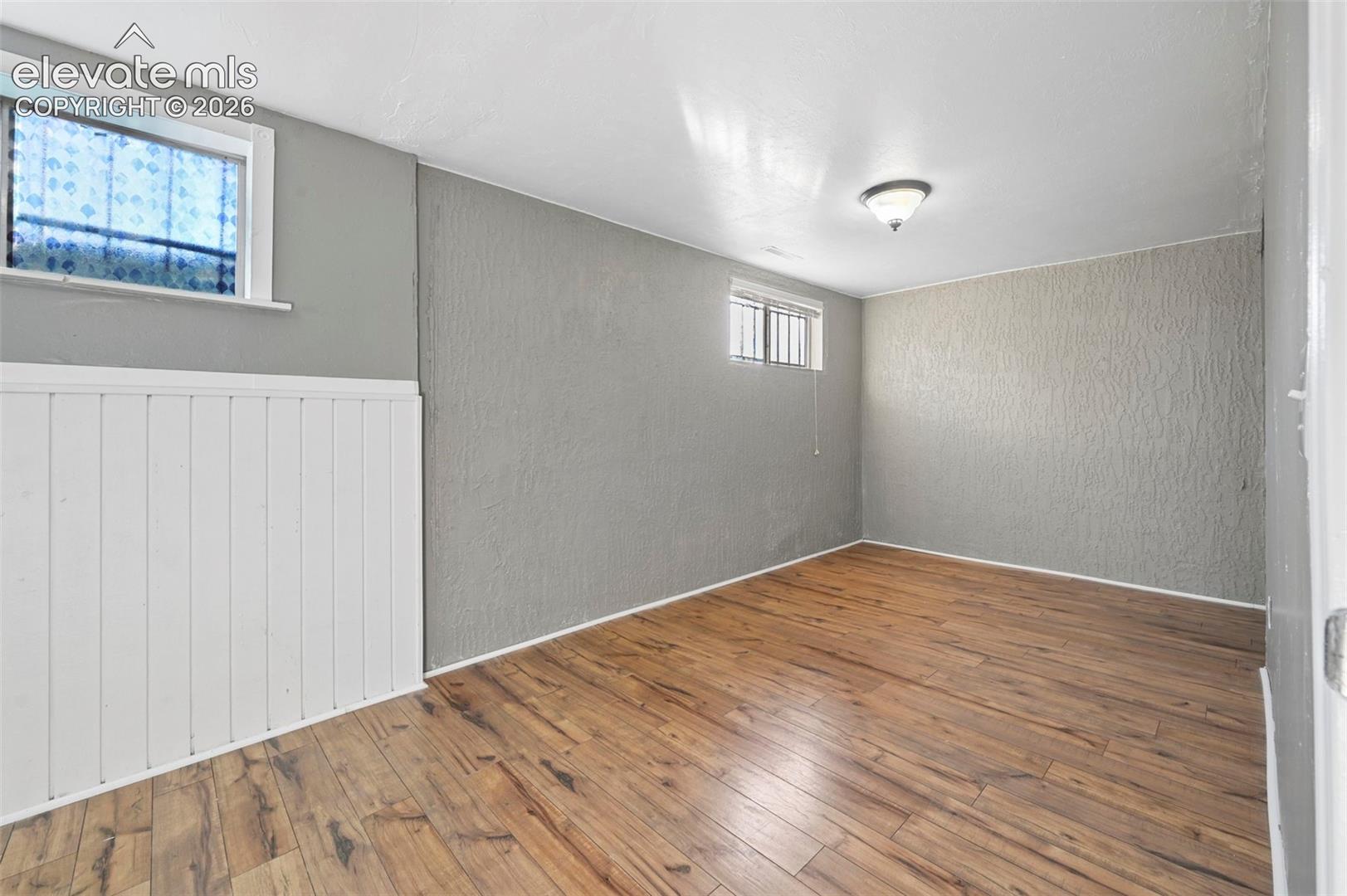 Unstaged bedroom in the basement that is so large/long that it could be an office!    Neutral-toned room featuring LVP flooring, white vertical wainscoting, textured wall surfaces, and two recessed windows 