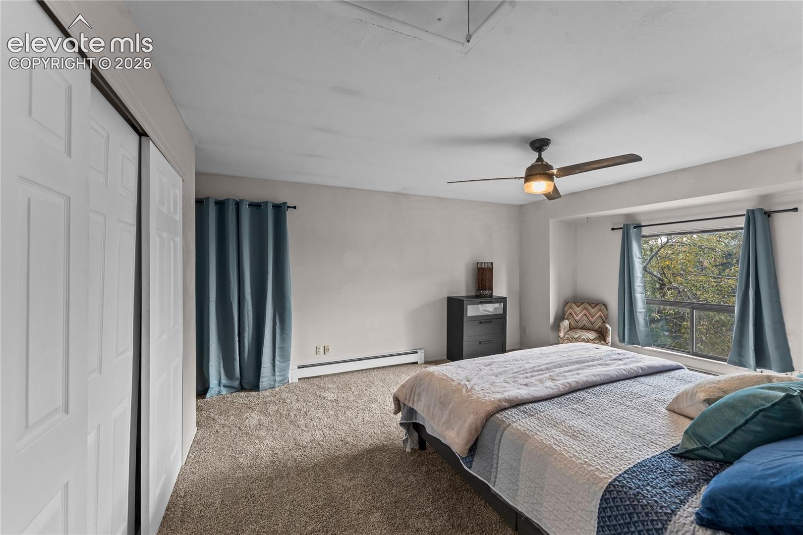Bedroom featuring carpeting, dual-panel sliding closet doors, a ceiling fan with integrated light fixture, and a window with a natural backdrop